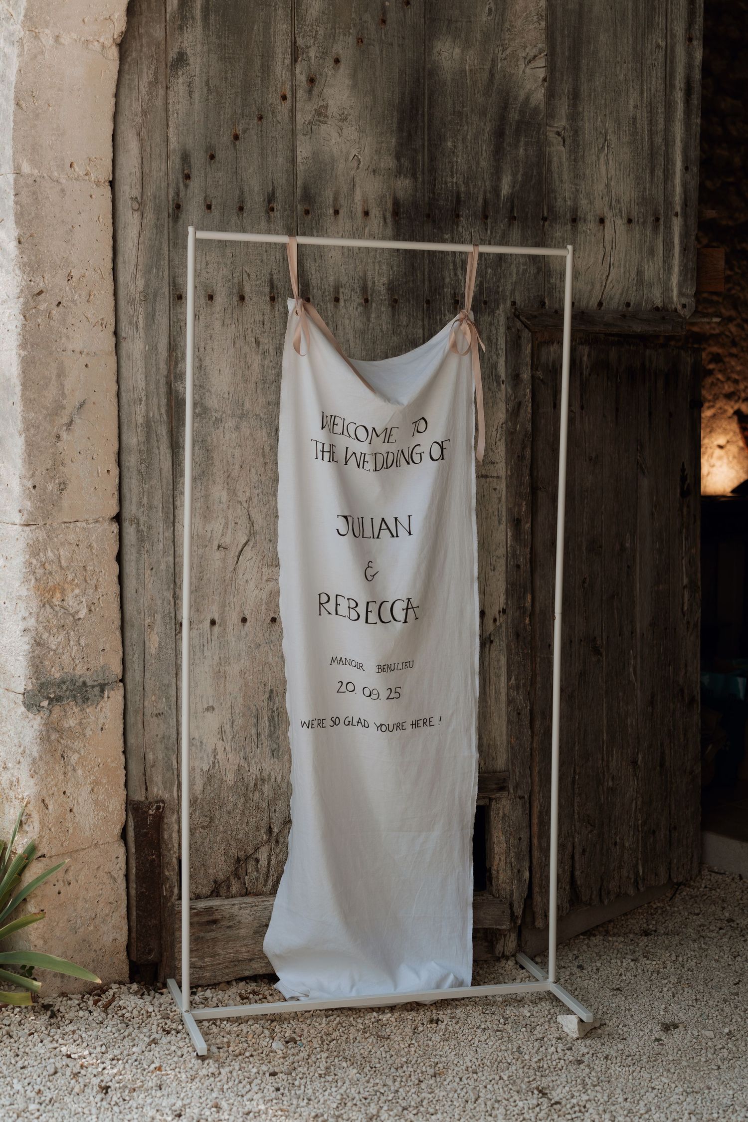 A white wedding dress hangs on a metal rack against a rustic stone wall with text details.