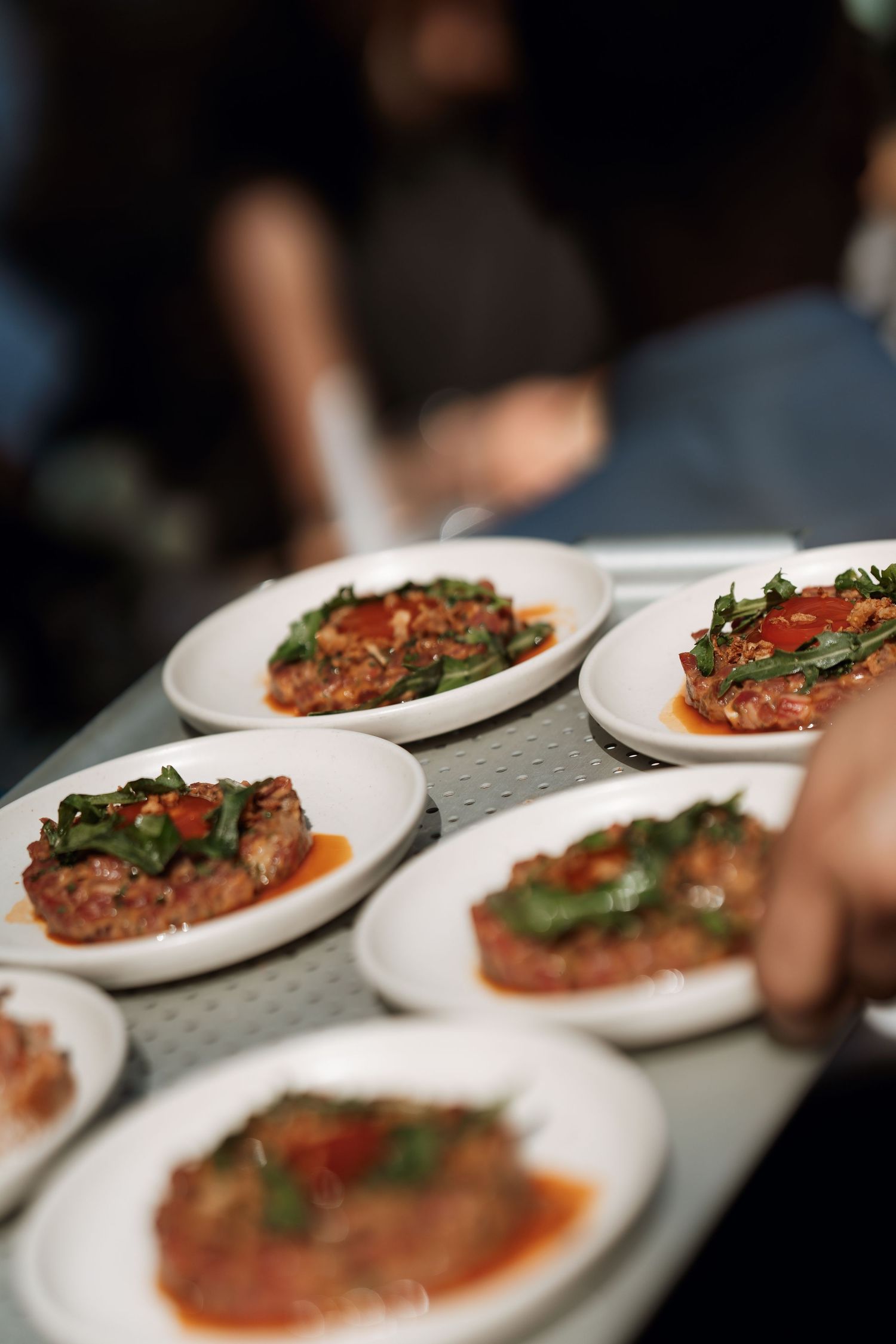 A row of elegantly plated dishes with garnished meat and sauce arranged on white plates.