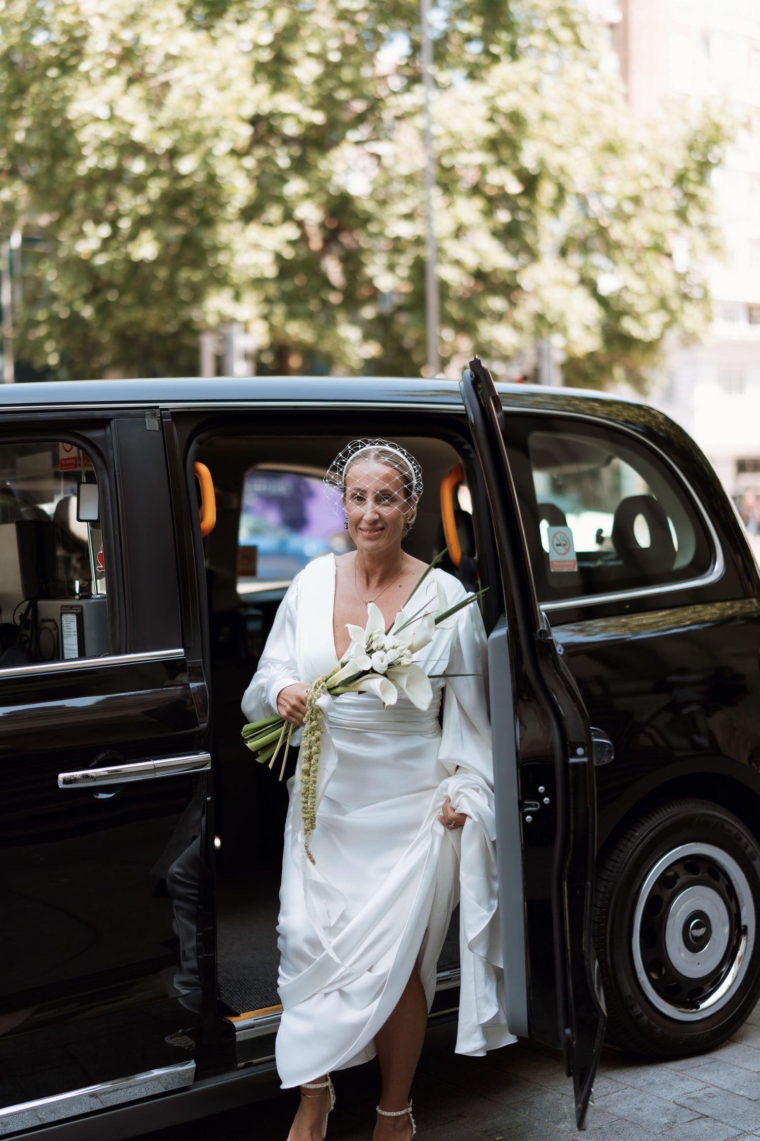A bride in white dress stepping out of a classic black London taxi cab.