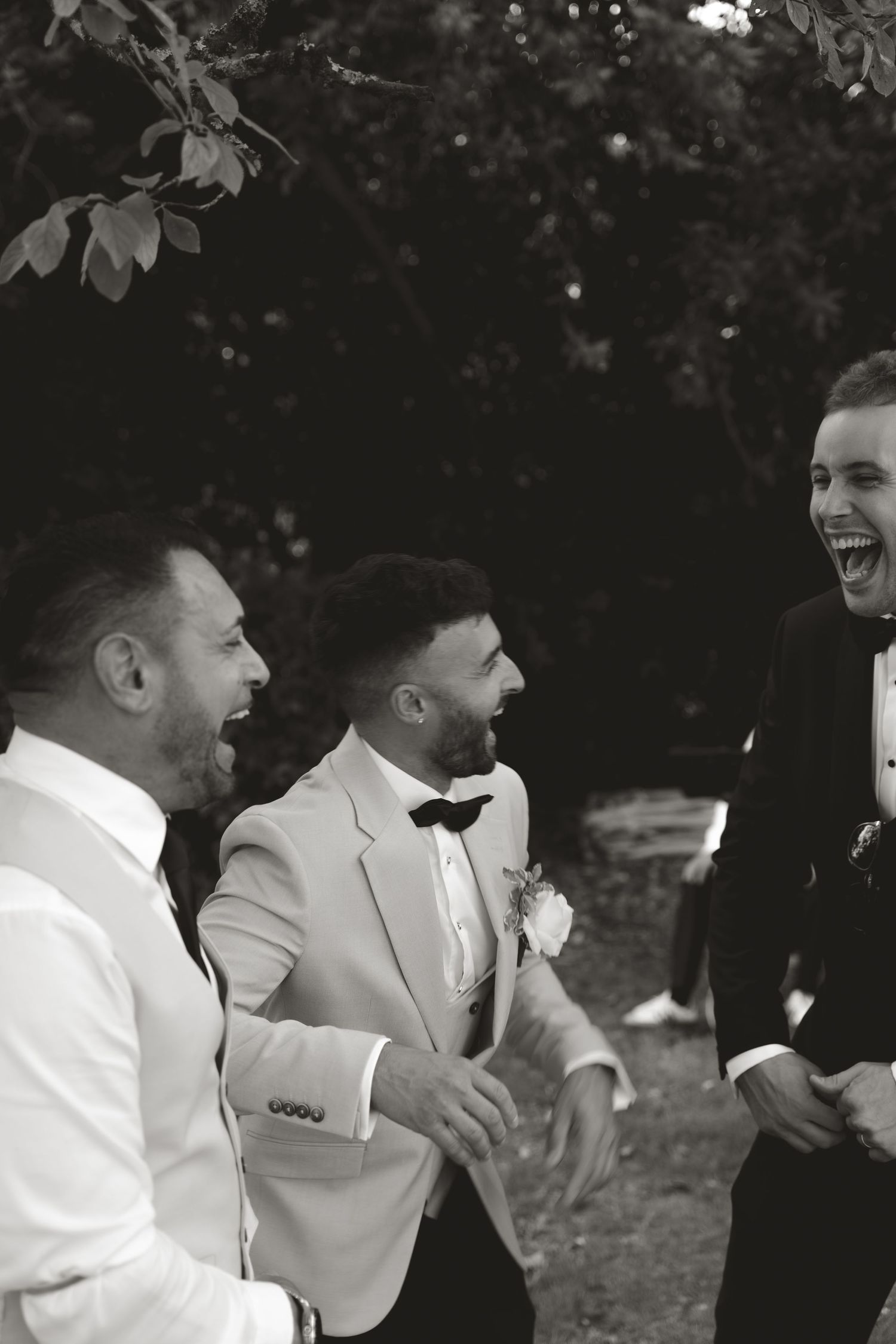 Black and white photo capturing joyful laughter among wedding party members outdoors.