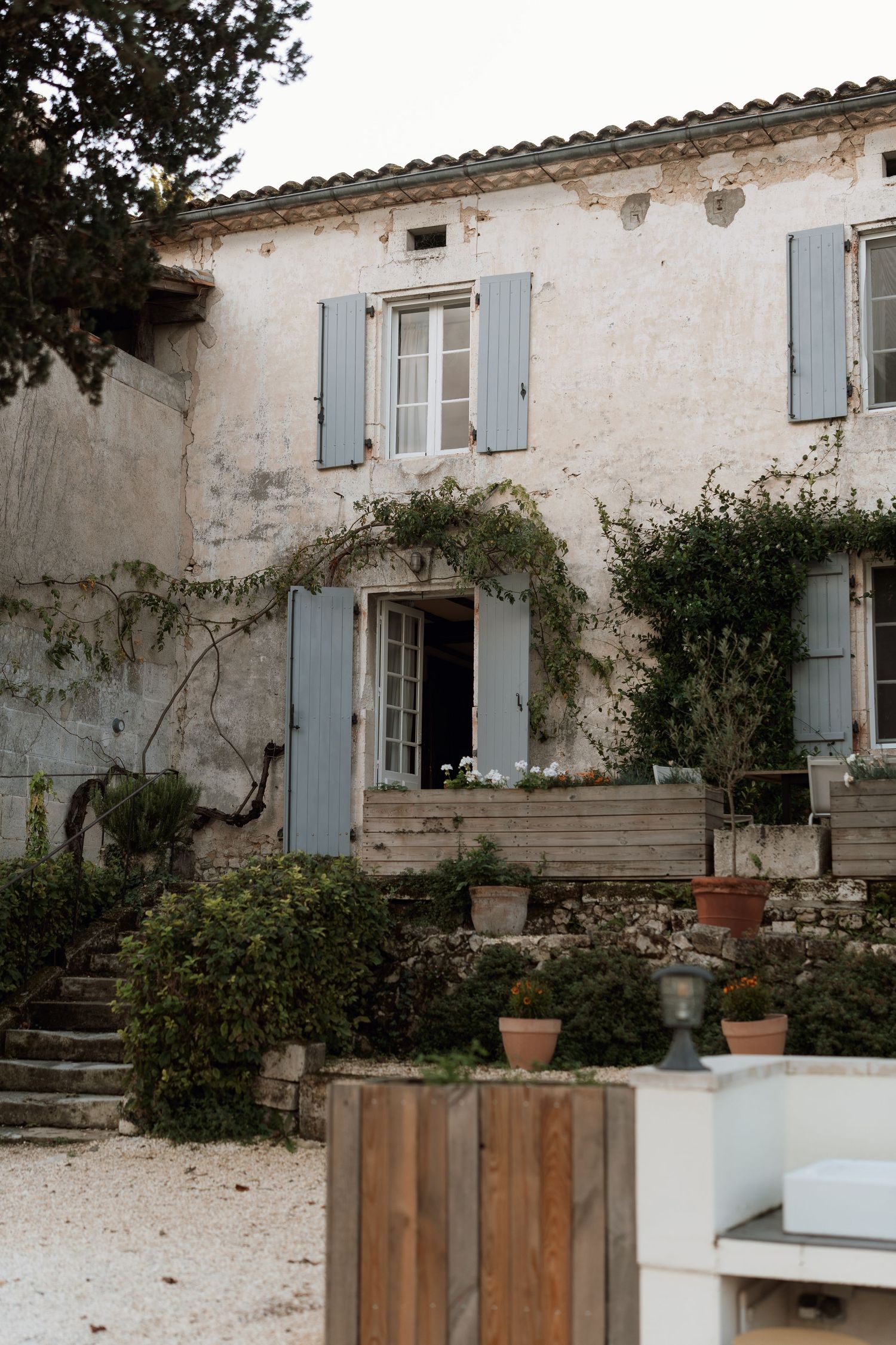 A charming white stone house with blue shutters and potted plants adorning the entrance.