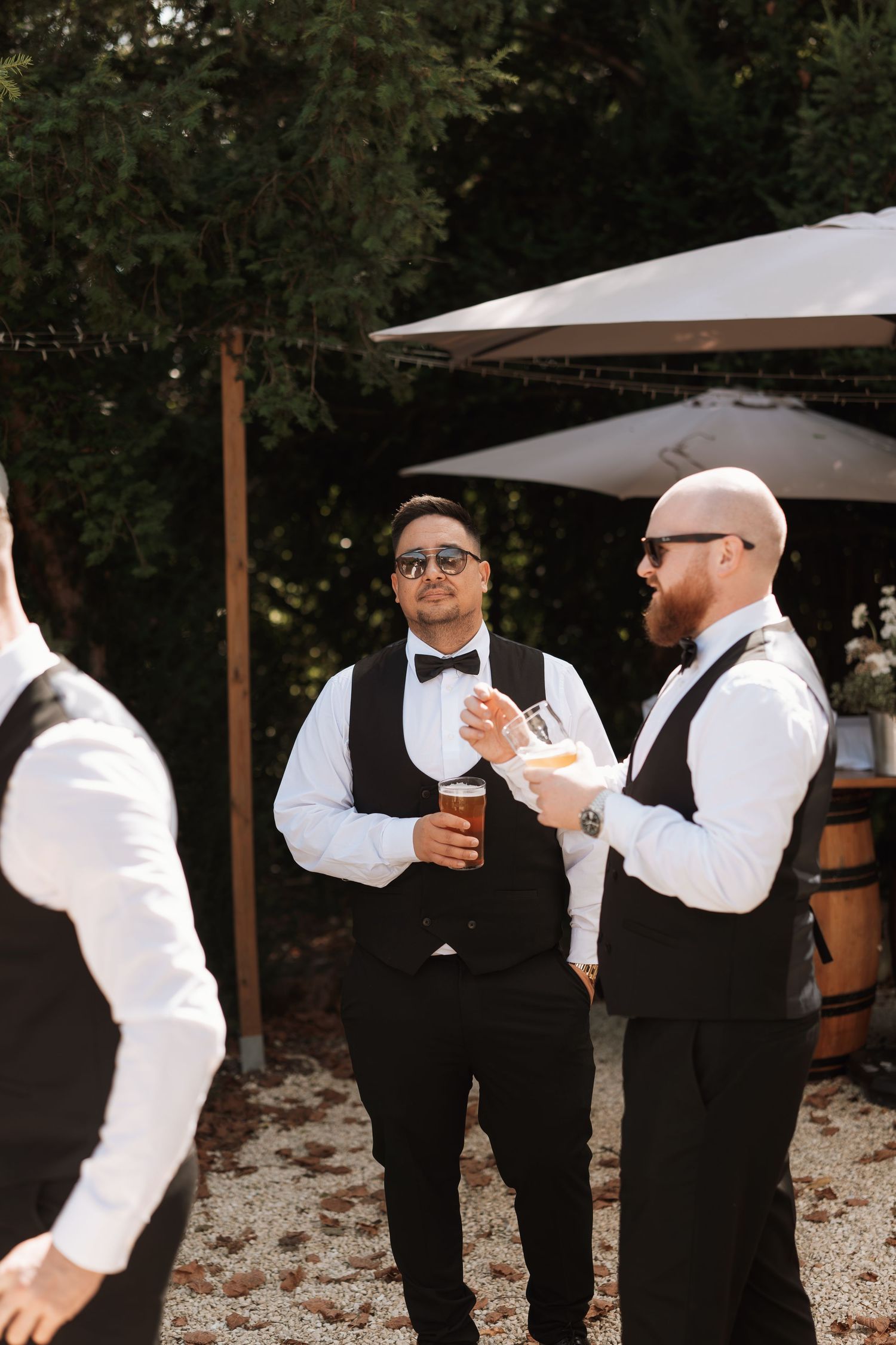 Wedding party members in black and white attire gather under outdoor canopies.