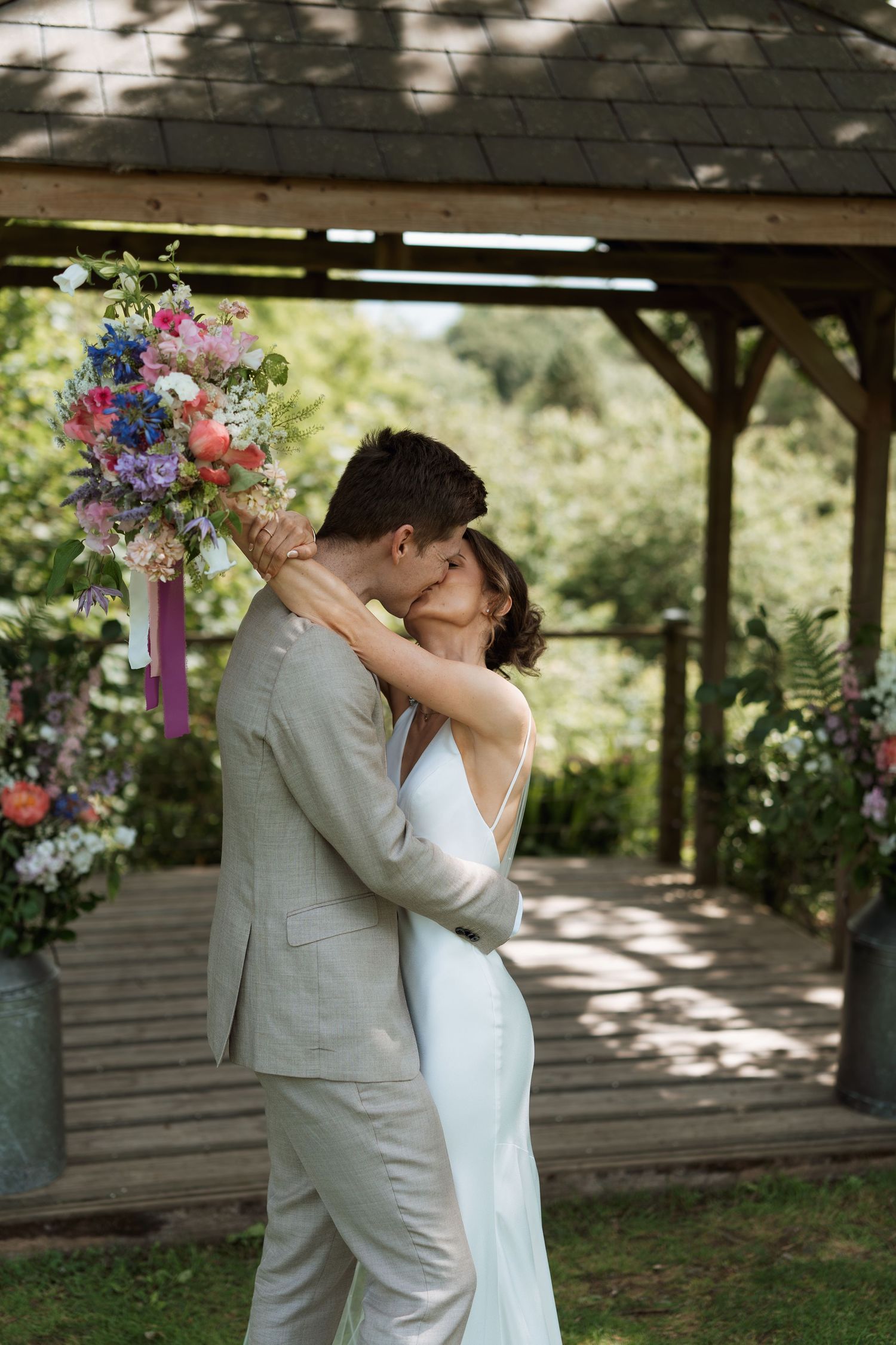 Newlyweds embrace and kiss in a series of romantic moments under a wooden pavilion.