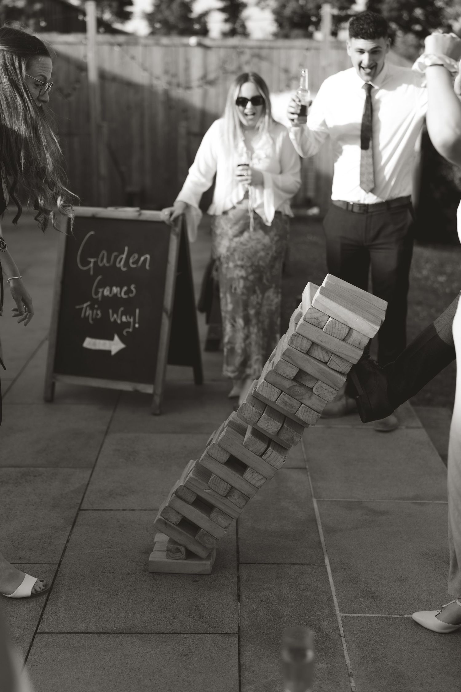 A black and white photo of wedding guests playing giant Jenga at an outdoor reception.