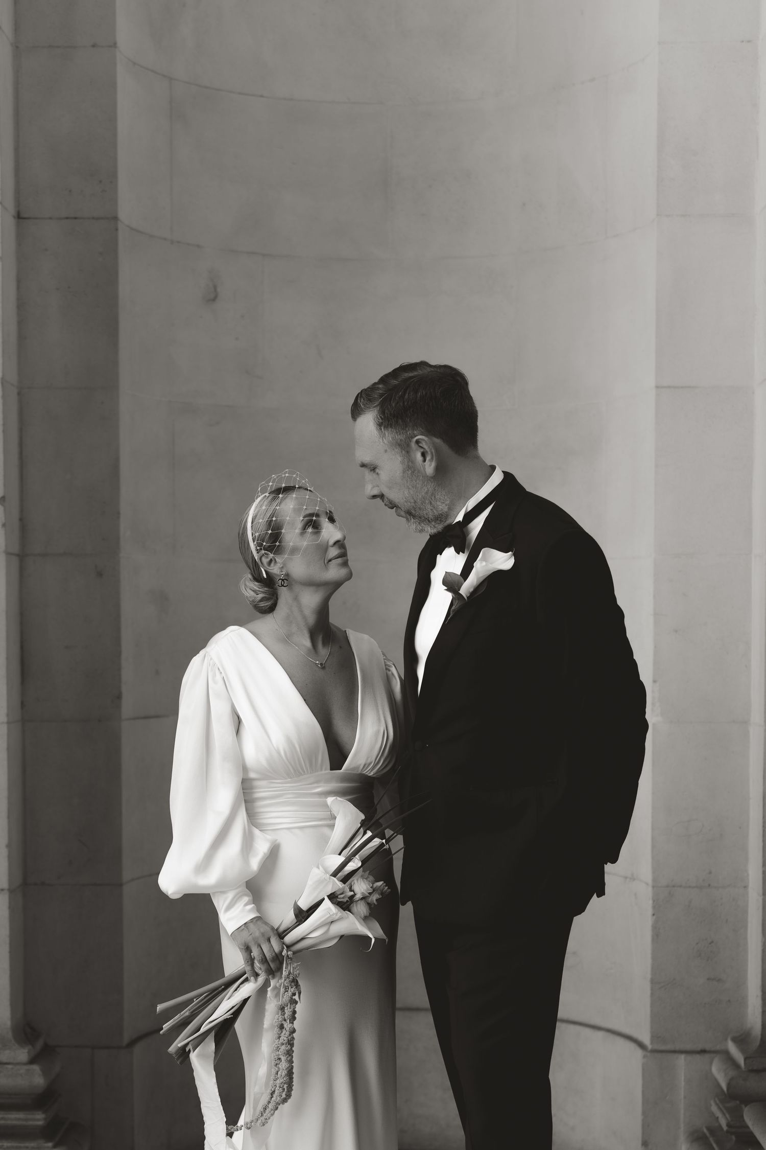 Black and white photo of a couple sharing an intimate moment between classical columns.