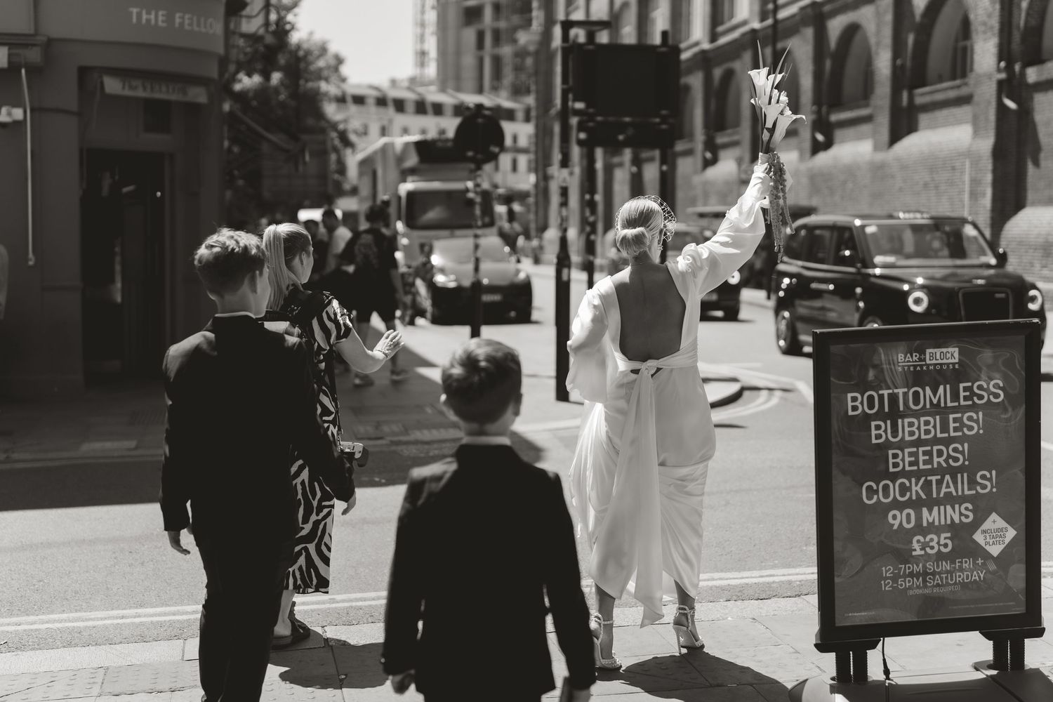 Black and white photo of a busy city street with pedestrians walking past storefronts and signage.