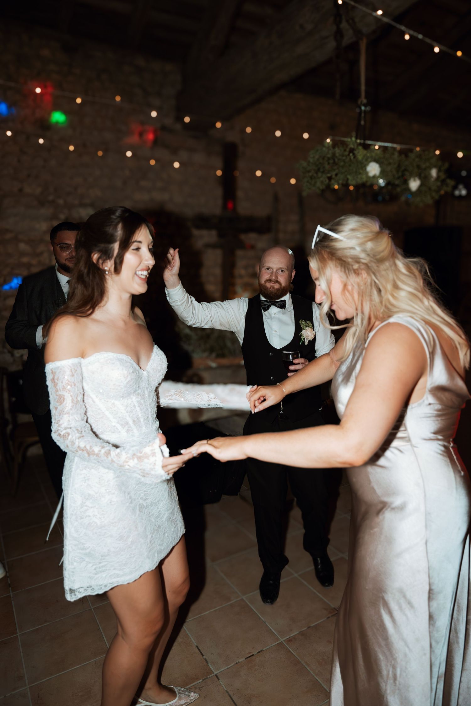 Wedding reception dance party with guests in formal attire under string lights.