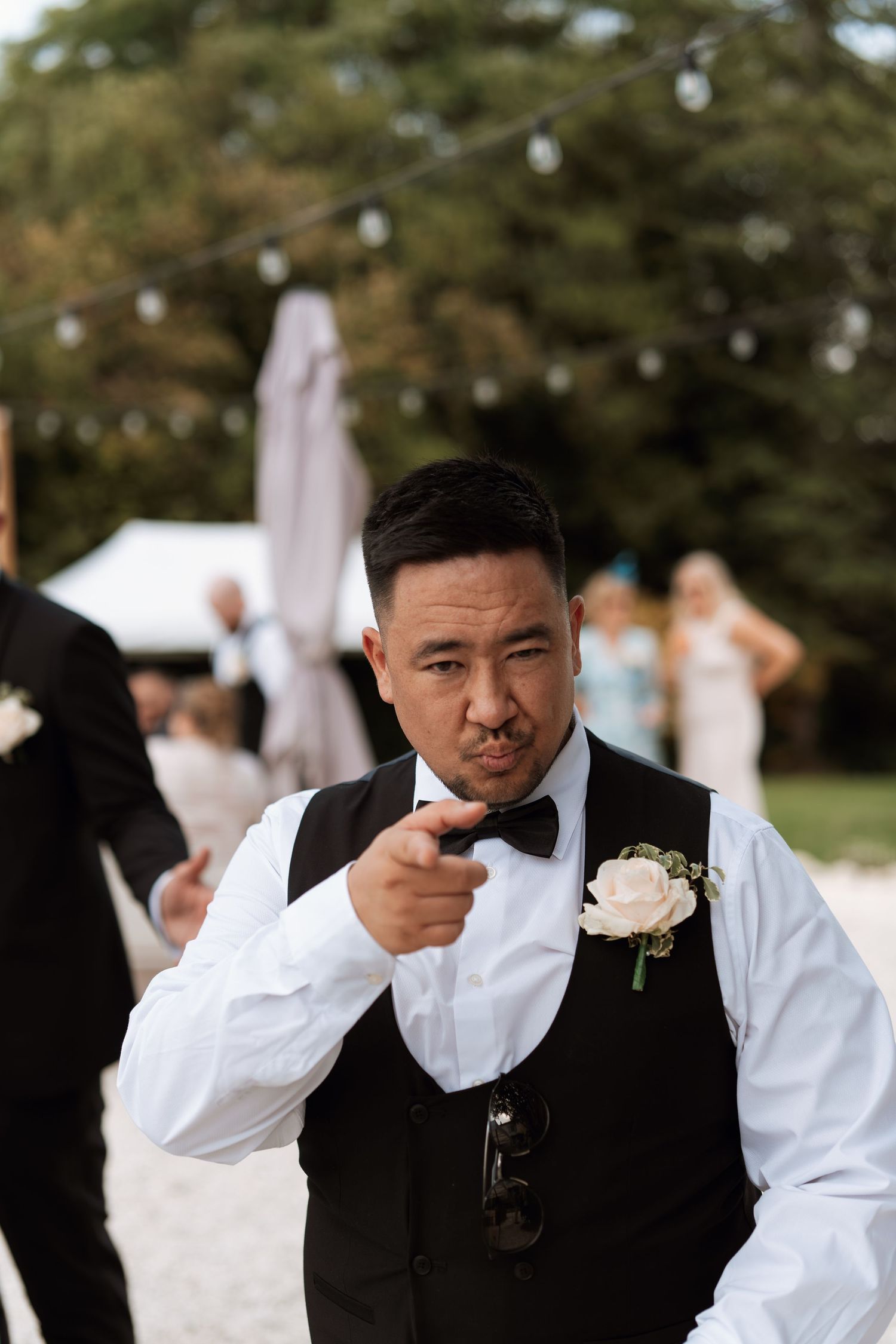 A groomsman in formal attire adjusts his bowtie during wedding preparations.