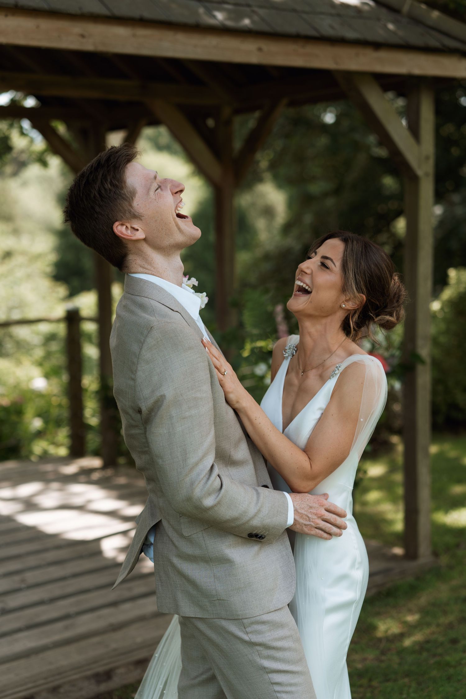 Joyful couple sharing a candid laughing moment under a wooden pavilion.