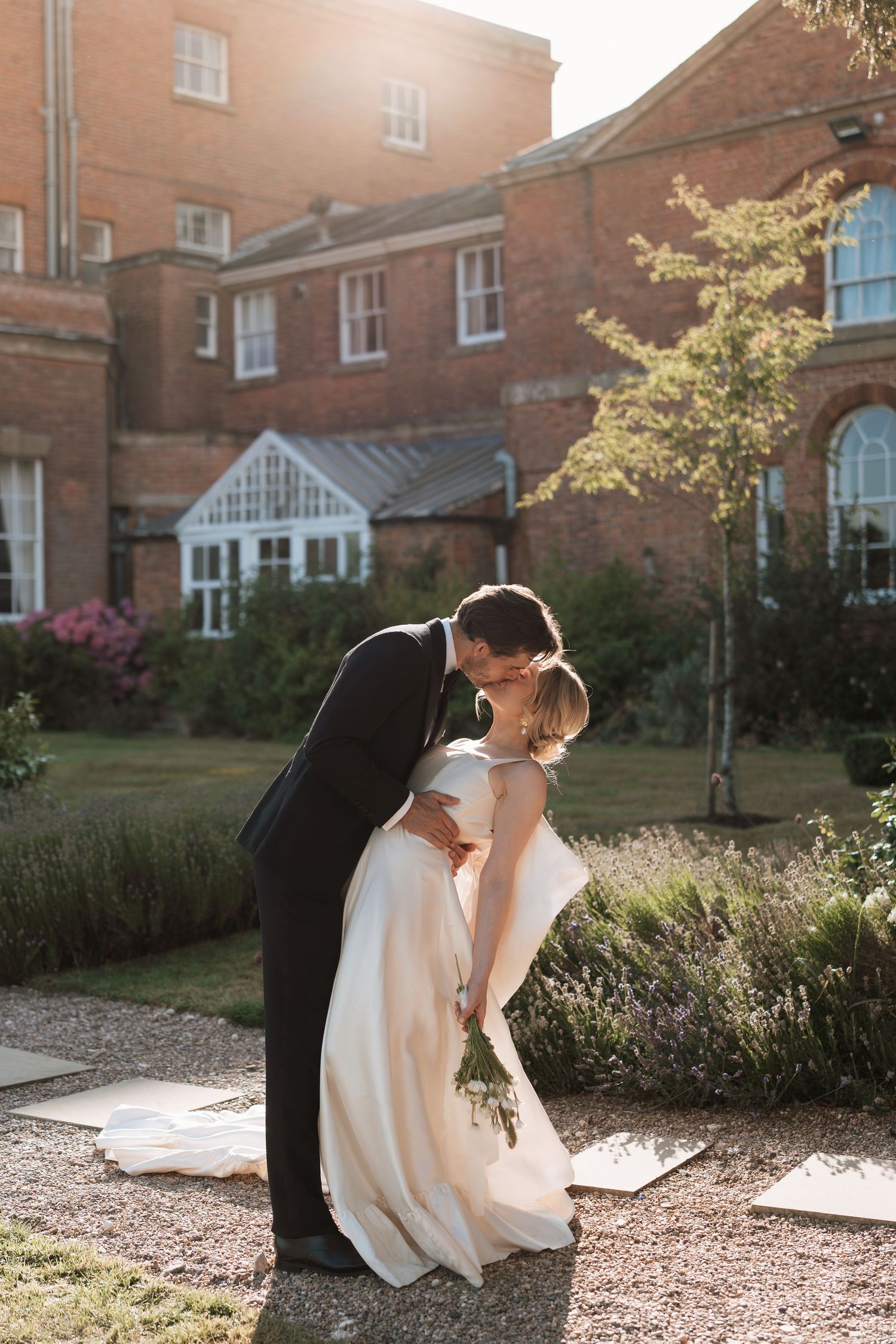A romantic couple shares a tender moment in golden sunlight outside a historic brick building.