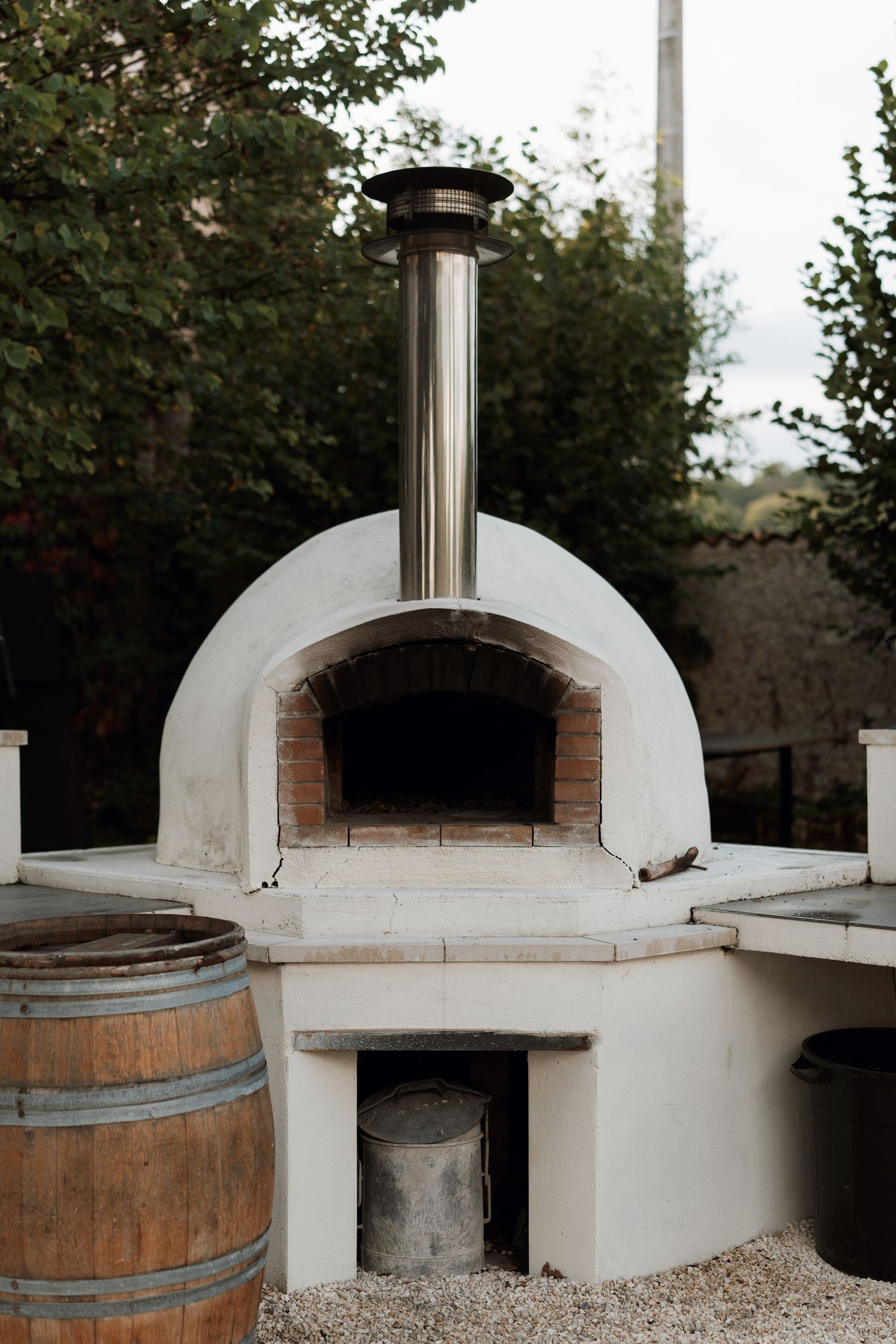 White stucco outdoor pizza oven with wooden barrel and curved design features shown from multiple angles.