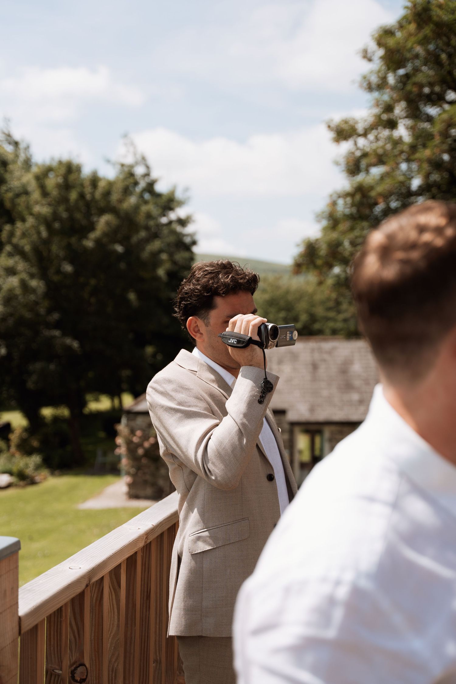 Photographer in beige suit capturing moments from wooden deck outdoors.
