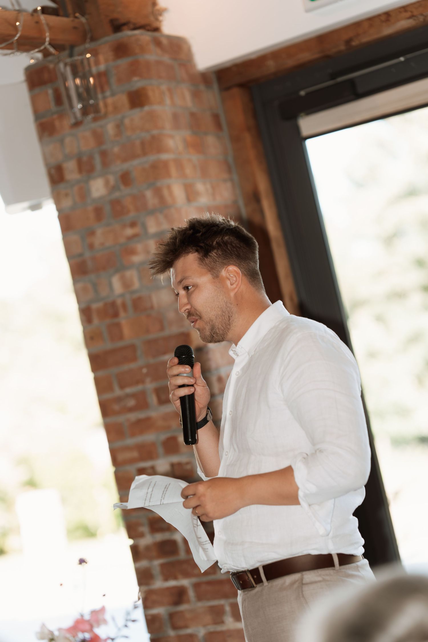 Speaker giving emotional wedding speech at rustic brick venue.