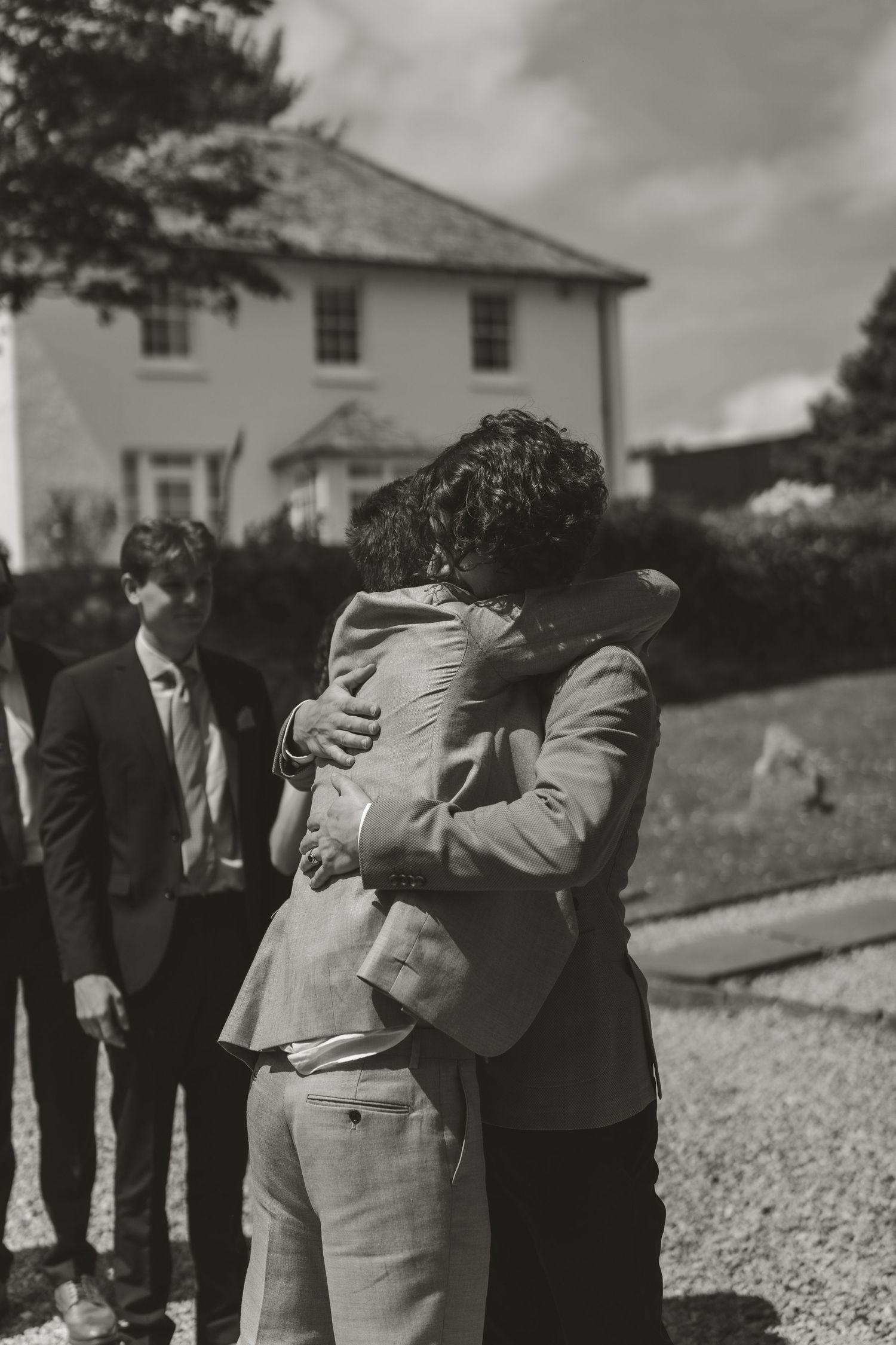Black and white photo showing groomsmen hugging and celebrating outdoors.