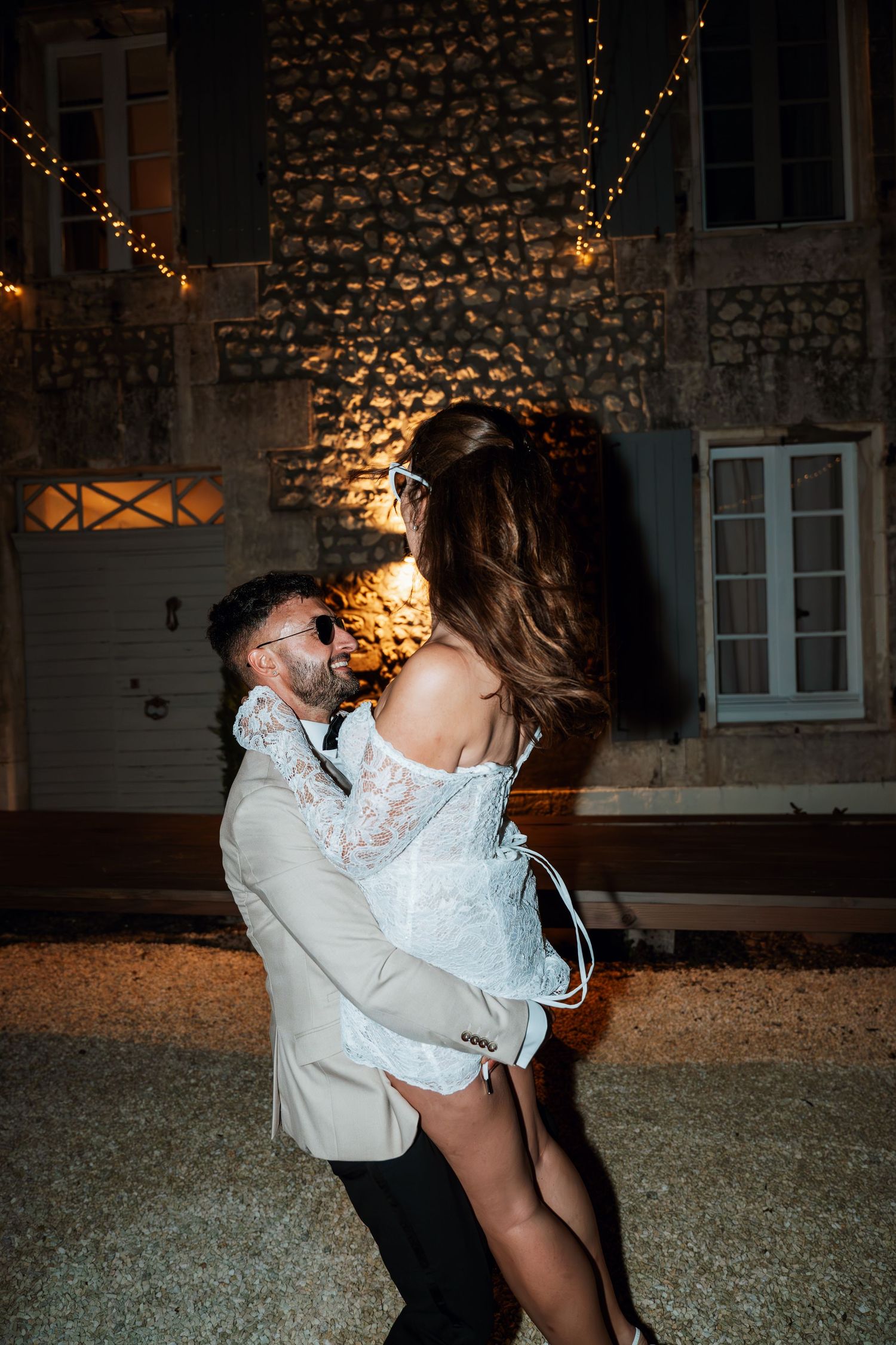 Couple shares an intimate dance moment against a stone wall lit by warm string lights.