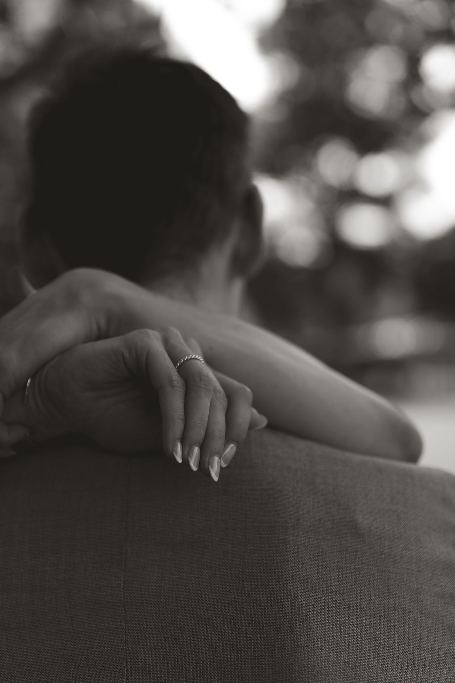 Black and white close-up photo showing hands resting on a textured fabric surface with a ring visible.