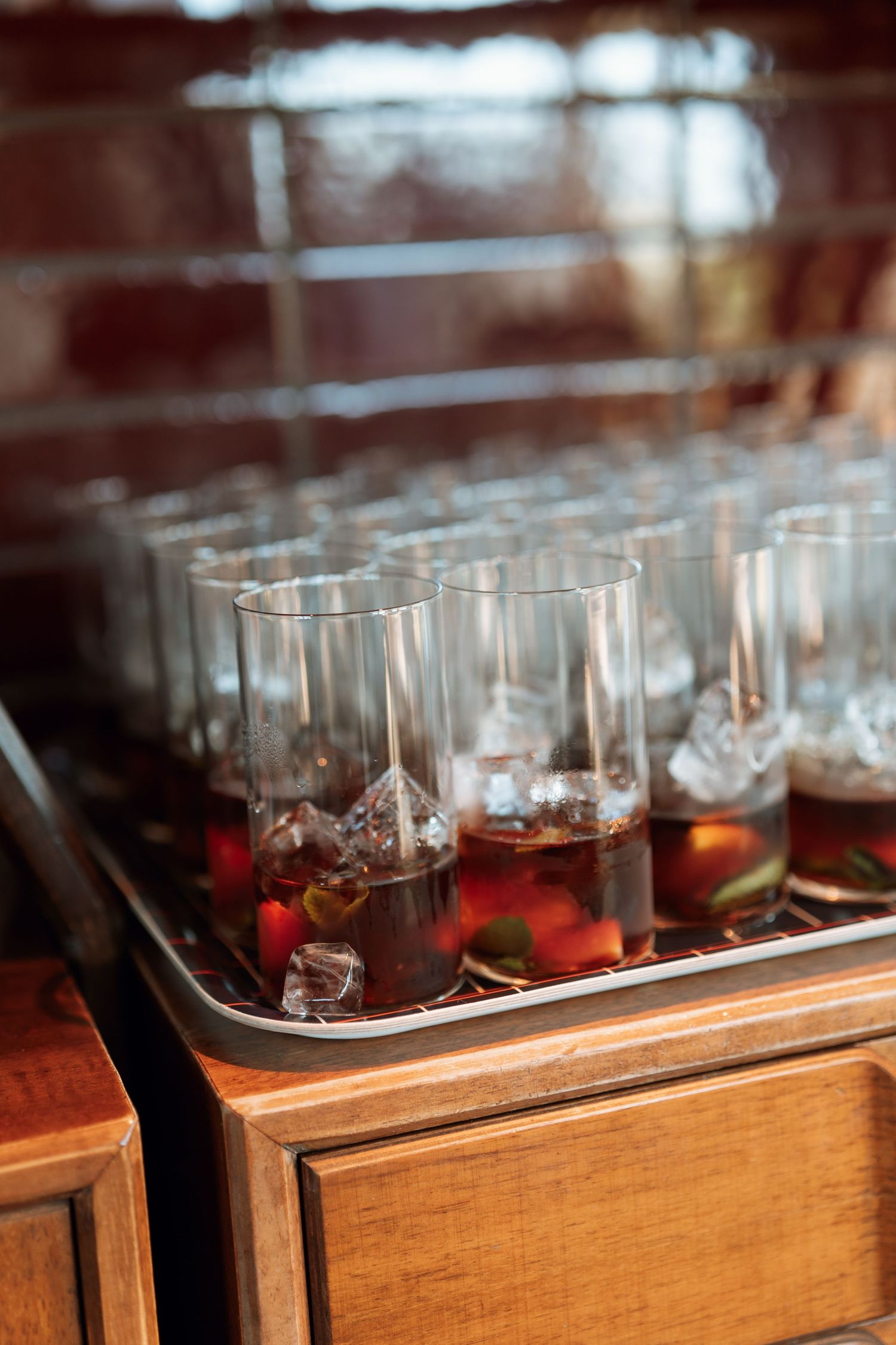 Elegant cocktails with ice cubes arranged in glasses on wooden serving tray.