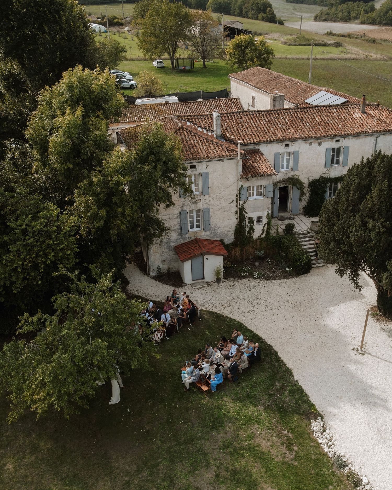 Aerial view of guests dining outdoors at rustic French countryside venue with terracotta roofs and gravel courtyard.