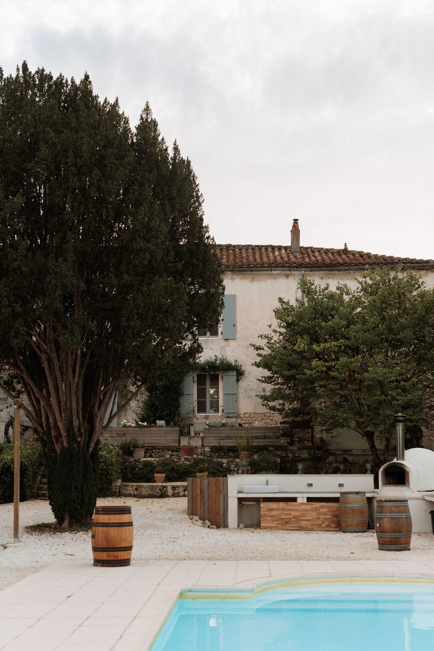 Modern villa exterior with swimming pool and wooden barrels surrounded by trees and greenery.