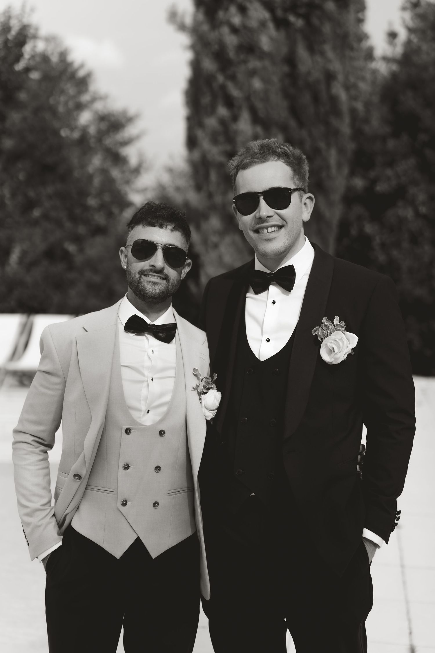 Groomsmen in formal attire and sunglasses pose for a black and white photo.