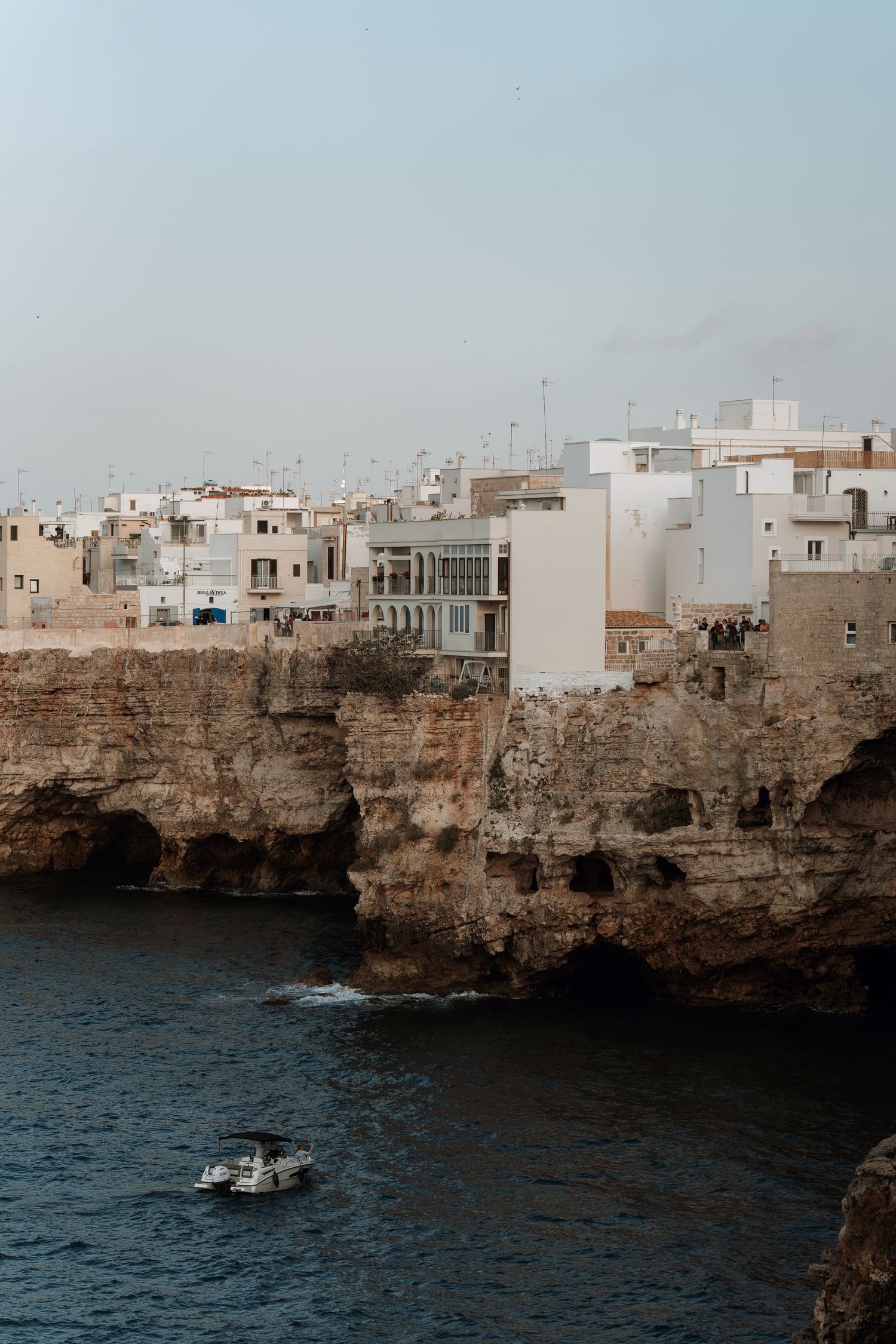 Coastal cityscape with white buildings perched on dramatic cliffs above blue waters.