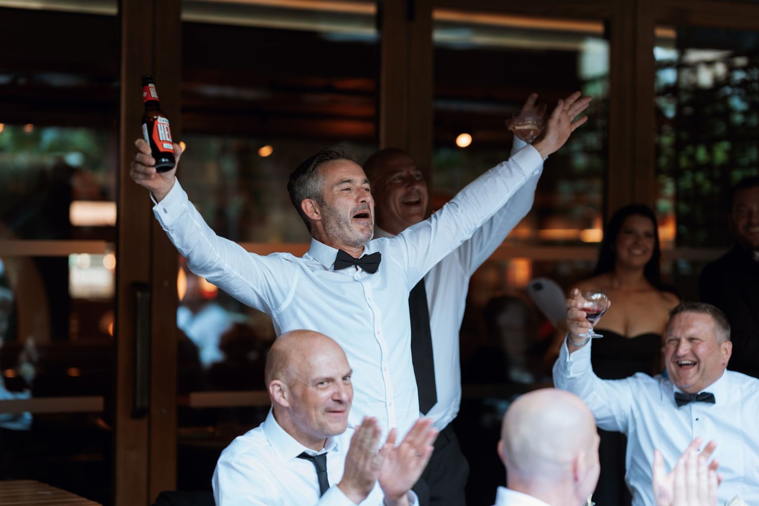 Celebratory moment at a wedding reception with guests cheering and raising their arms in excitement.