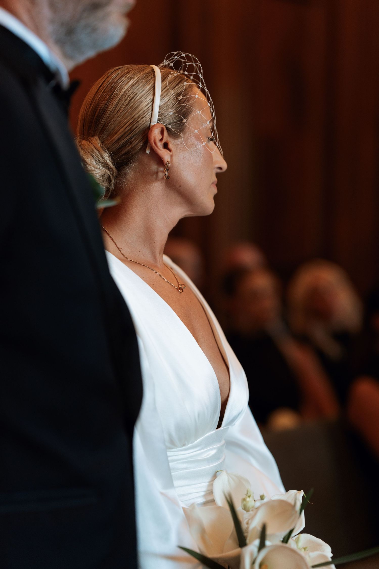 Elegant bride in a white dress holding a bouquet of white roses against a dark background.
