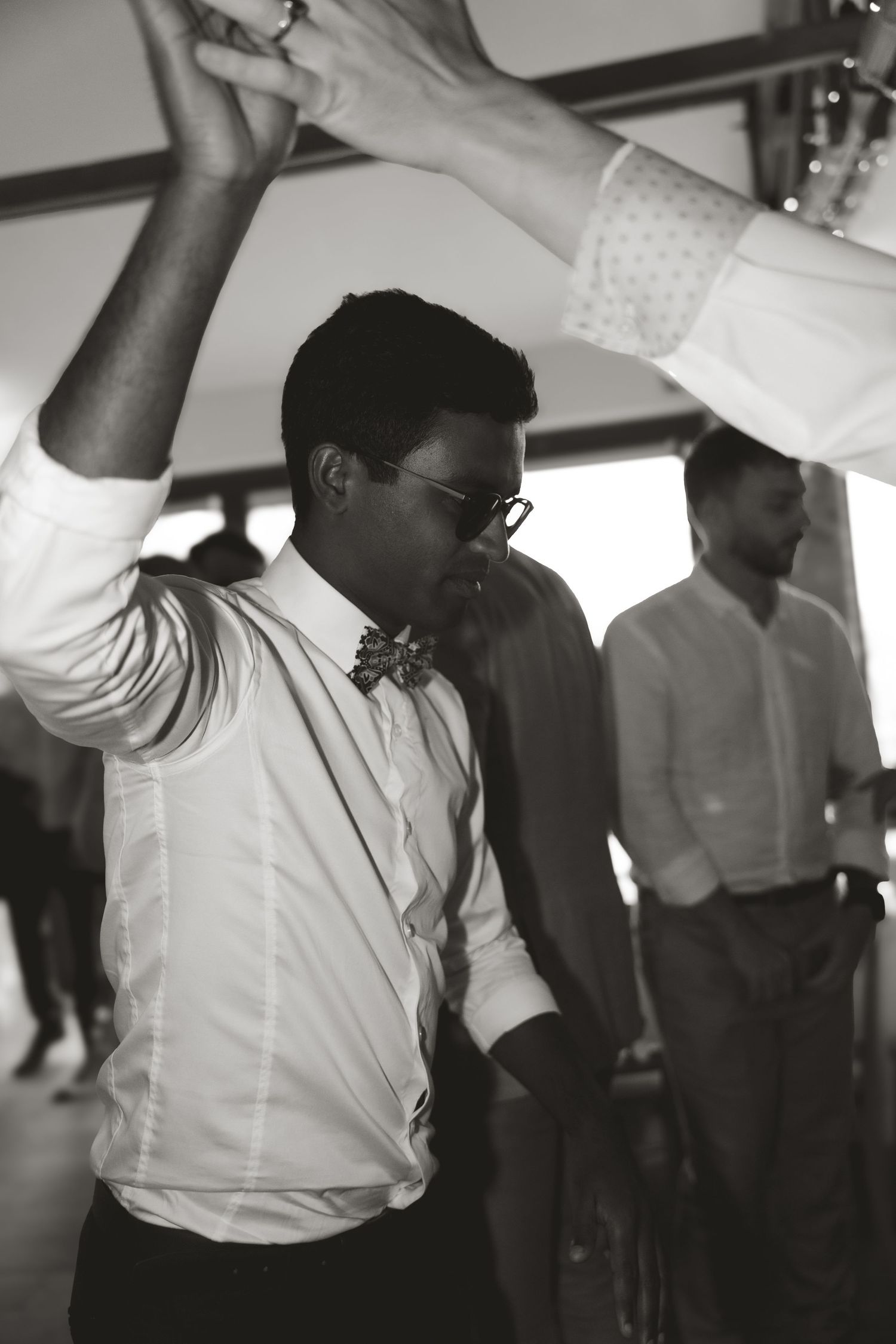 A guest in a bow tie and white shirt dances energetically at a wedding reception in black and white.