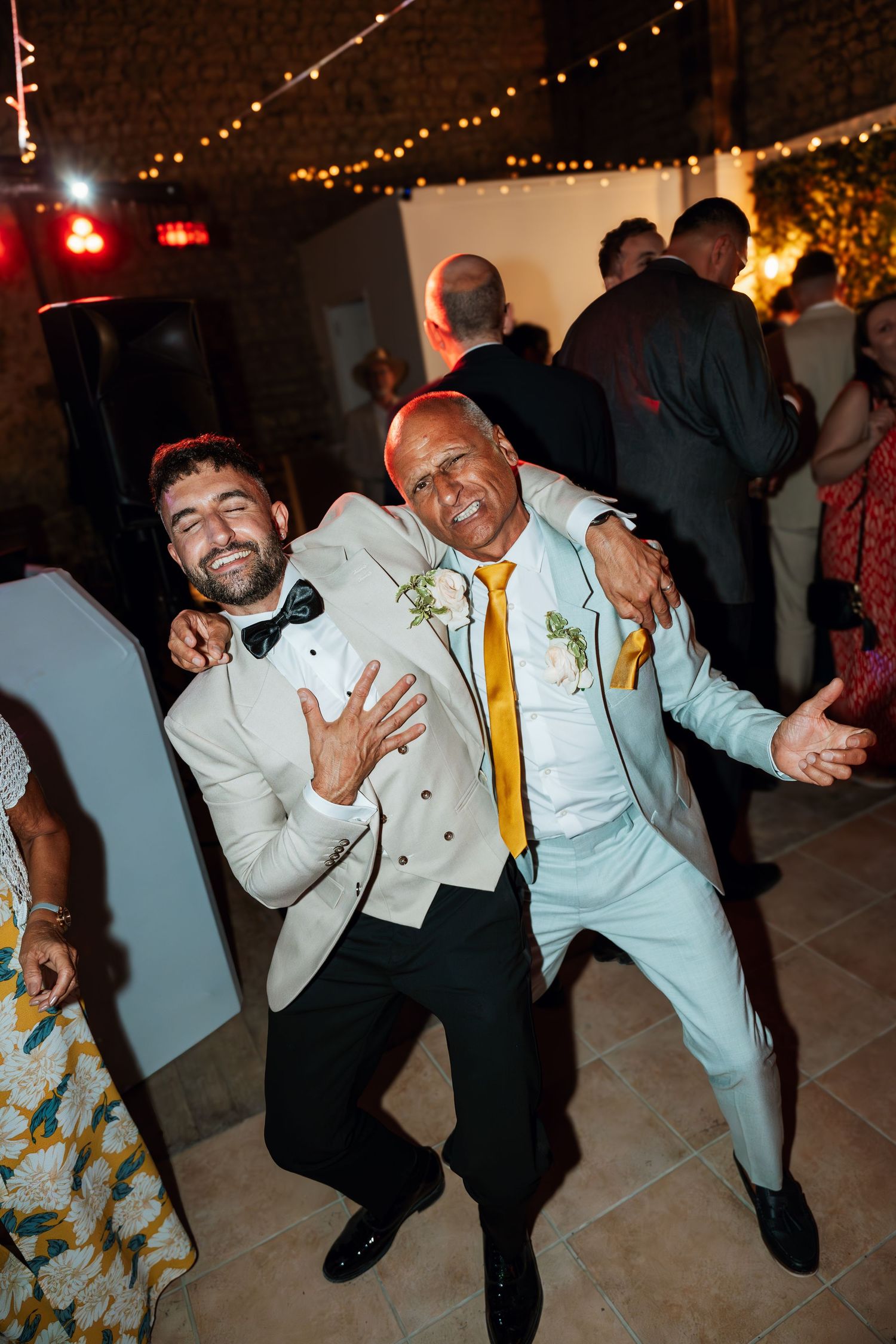 Wedding party members in white suits and yellow ties dancing and celebrating at a reception.