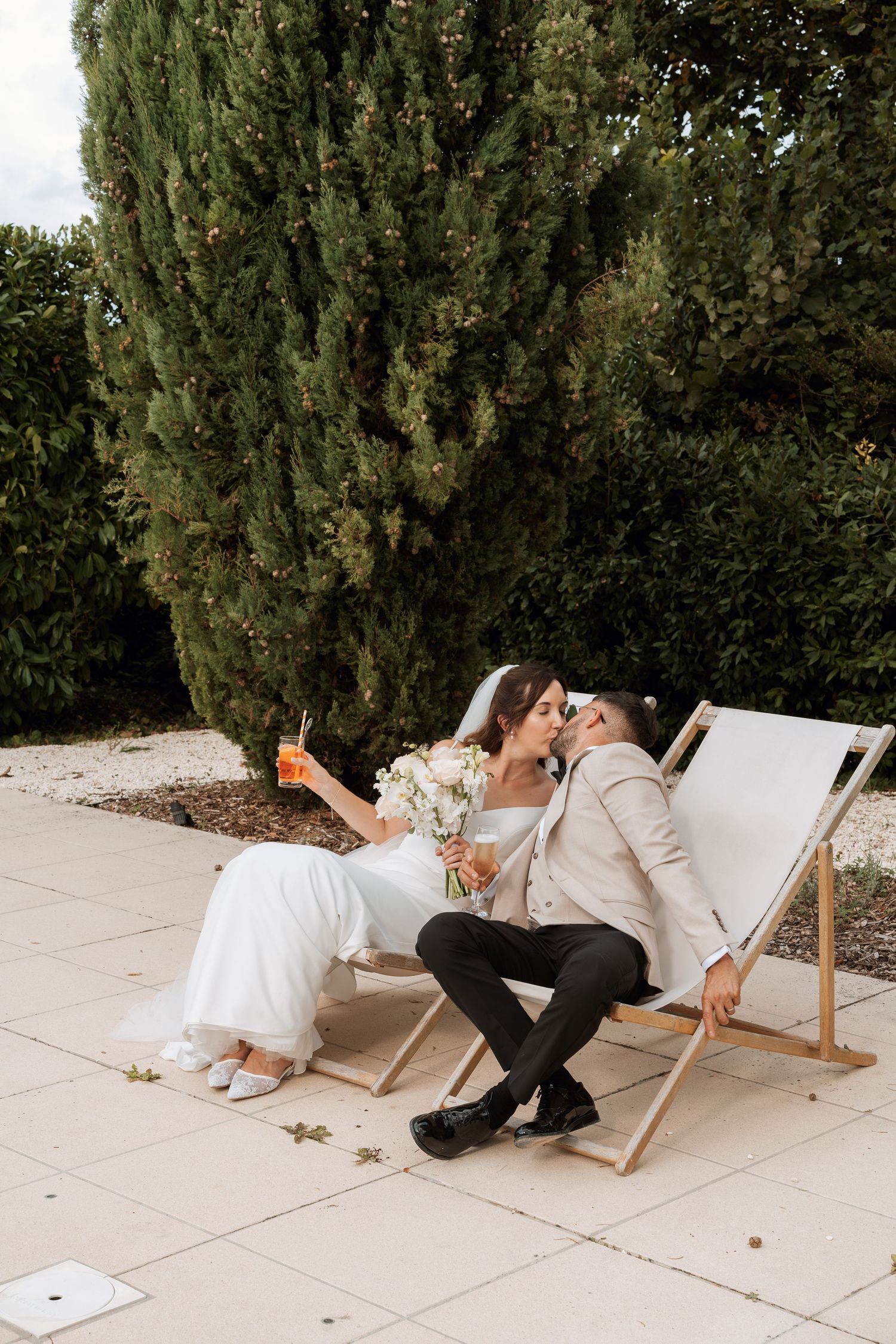 Couple relaxing in white deck chairs during an outdoor wedding celebration.