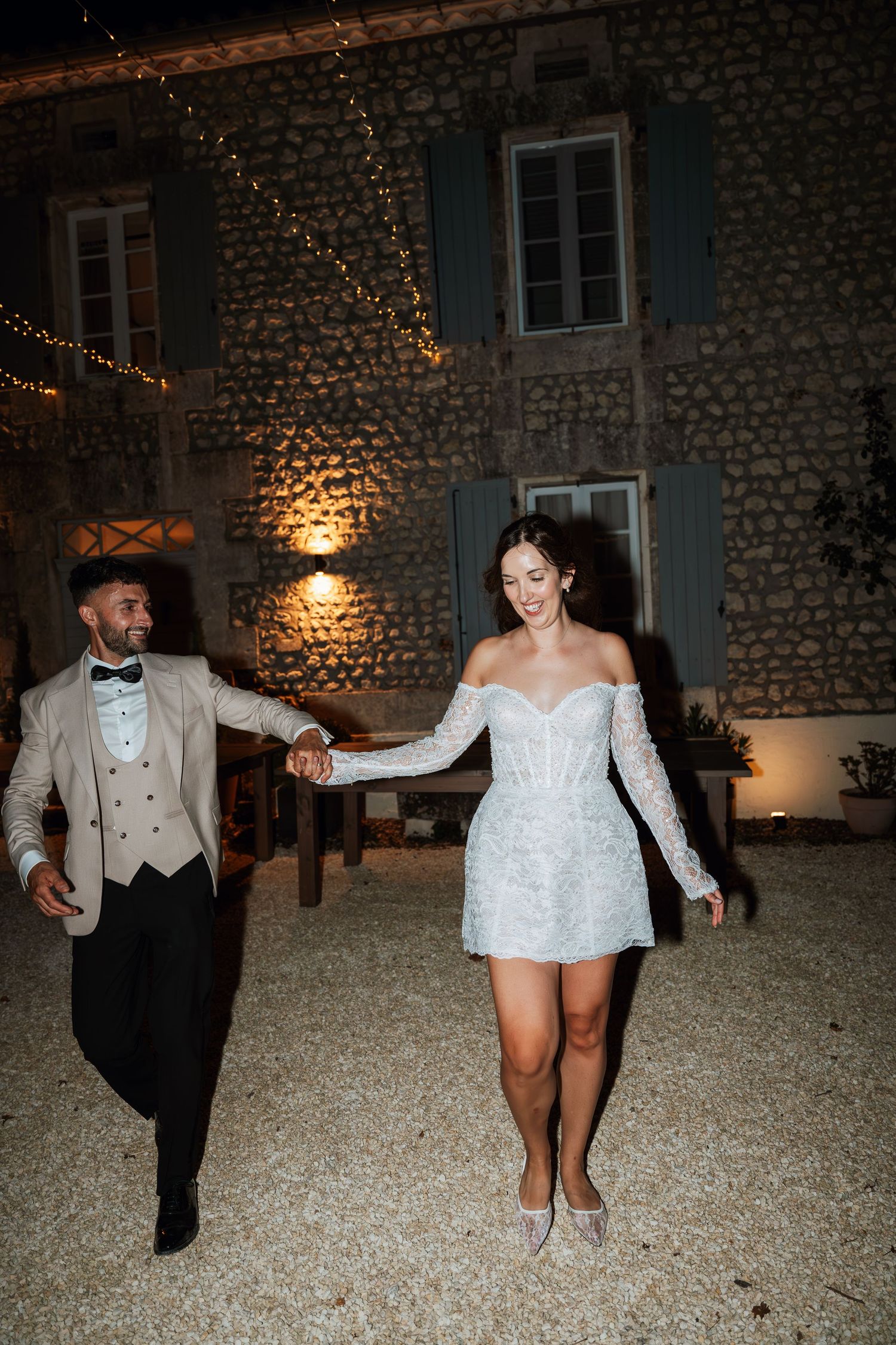 Couple dances energetically on gravel courtyard at night with stone building backdrop.
