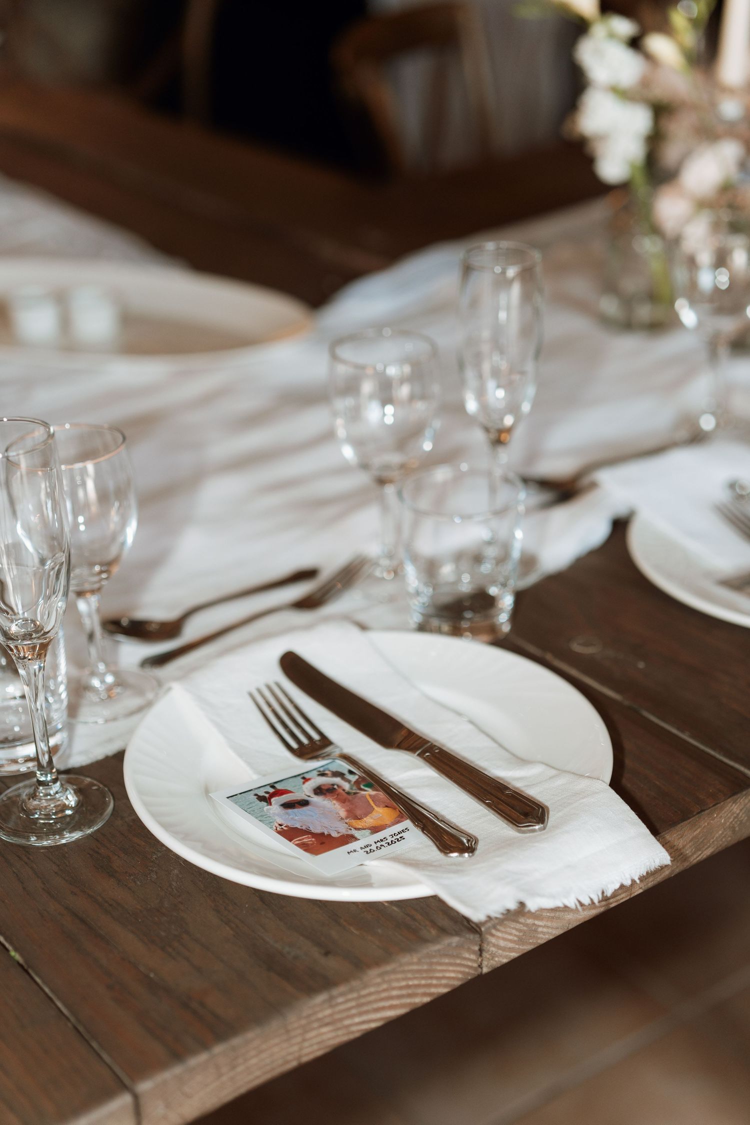 Elegant place settings with white plates and wine glasses arranged on a rustic wooden table.
