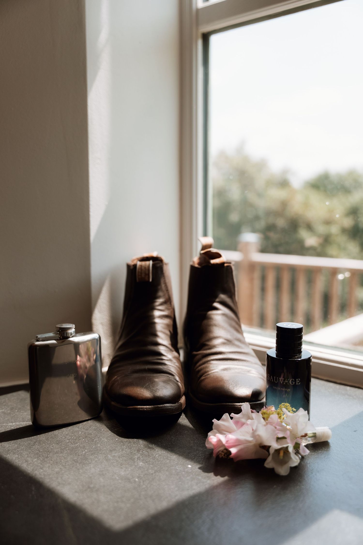 Brown leather dress shoes sit on a windowsill with delicate pink flowers in natural light.