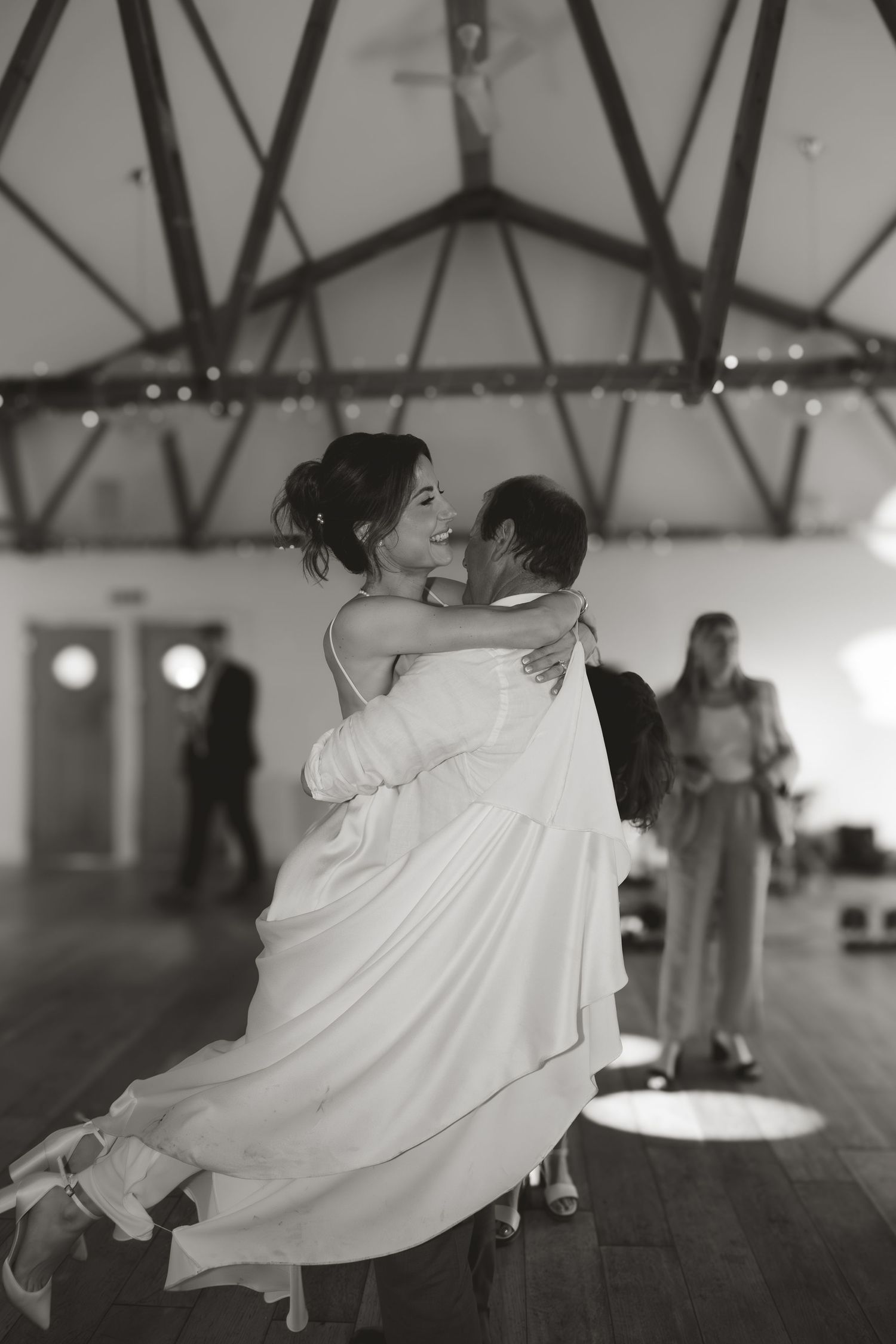 Black and white photo of couple dancing in spacious venue with exposed beams.