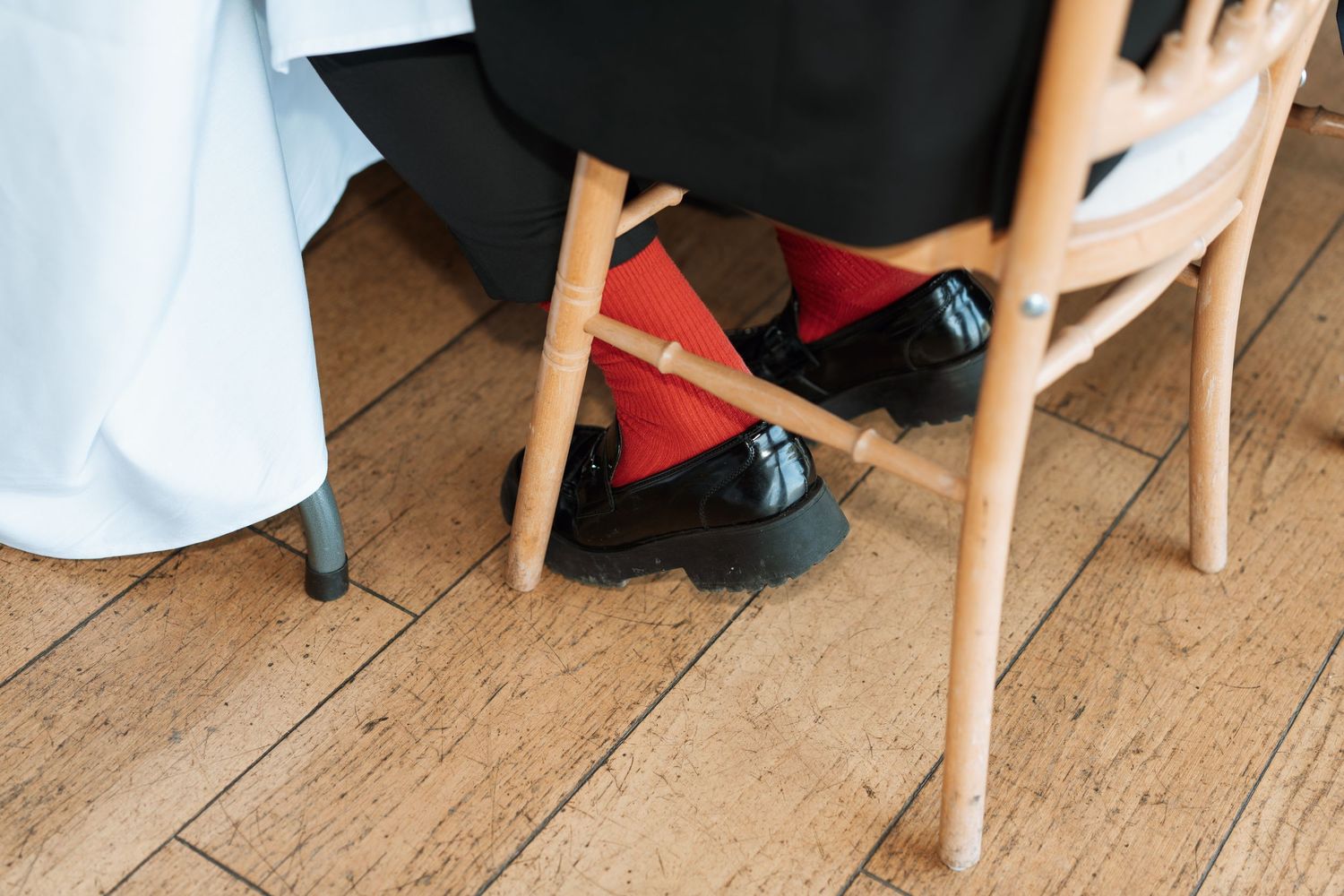Close-up view of wedding guests' feet and chairs on wooden flooring at reception.