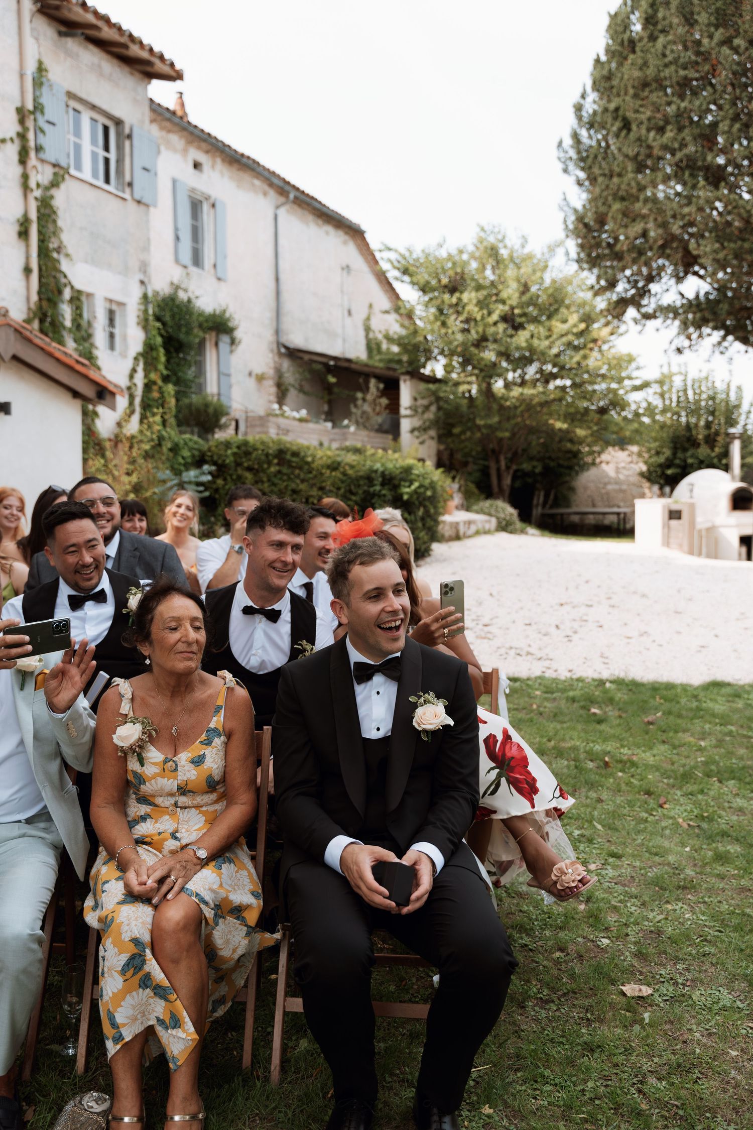 Wedding celebration outdoors with guests seated on wooden chairs enjoying the festivities.