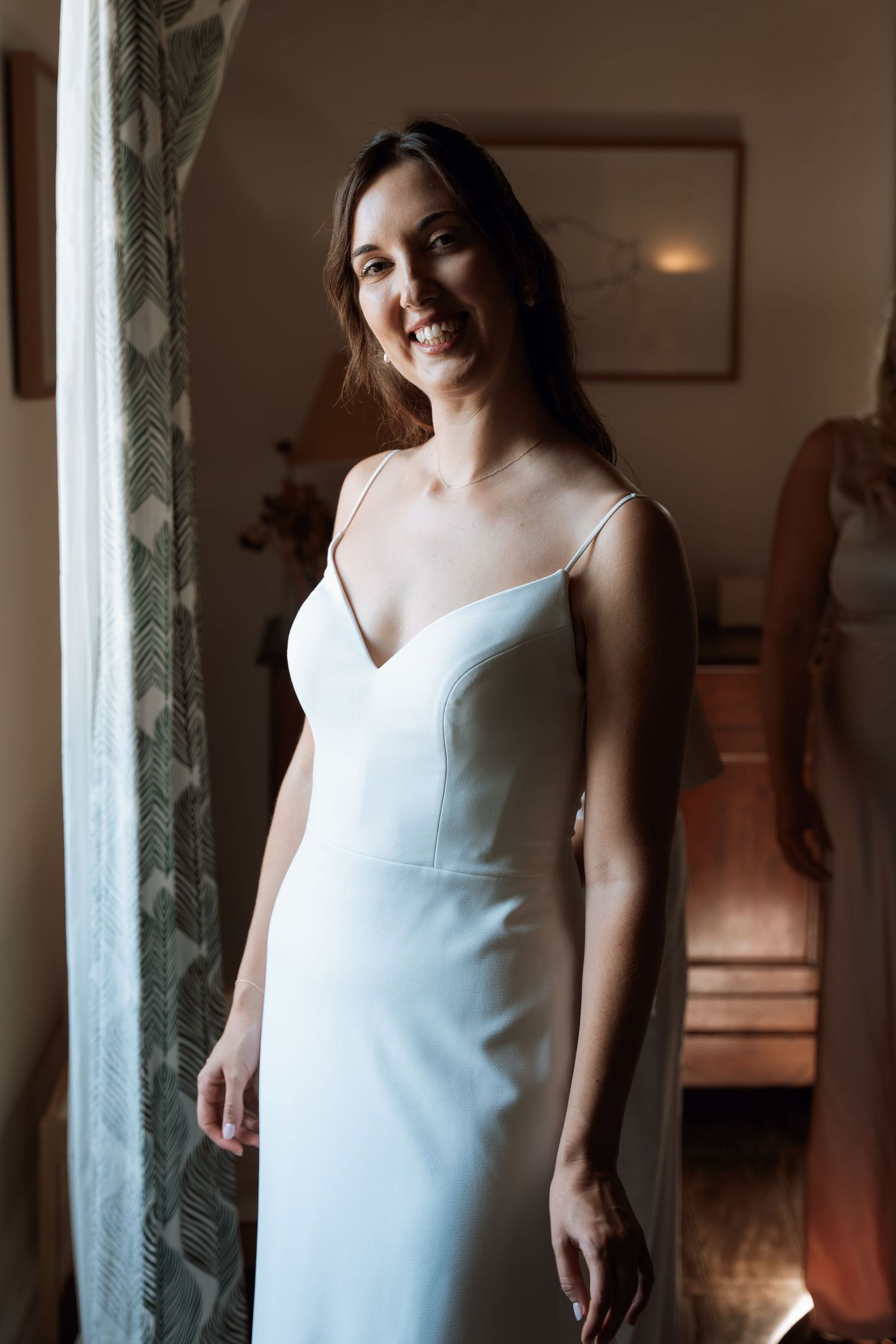 Woman in an elegant white dress standing in an interior space with decorative columns.