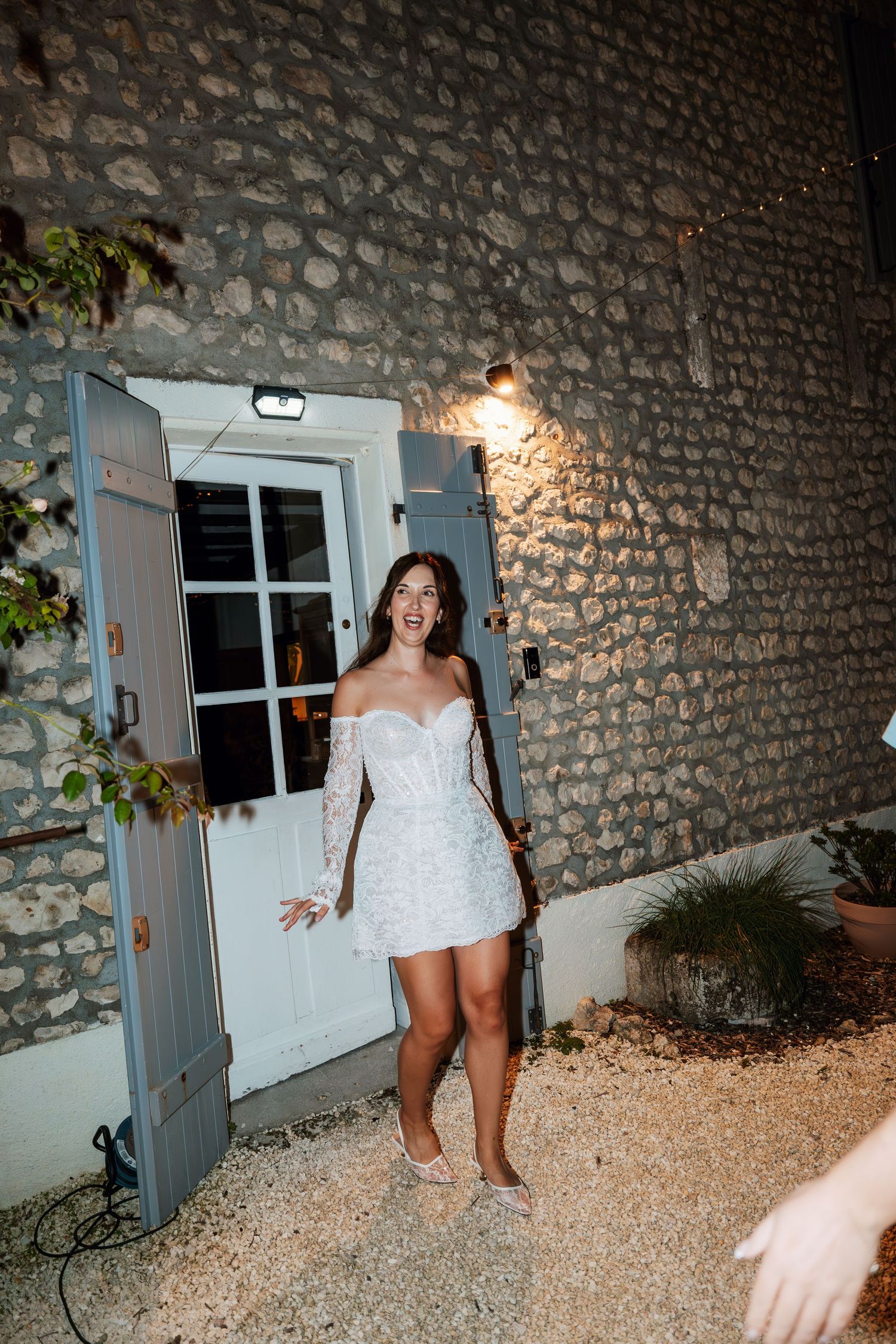 Person in white dress walking along stone wall exterior with blue doors at night.