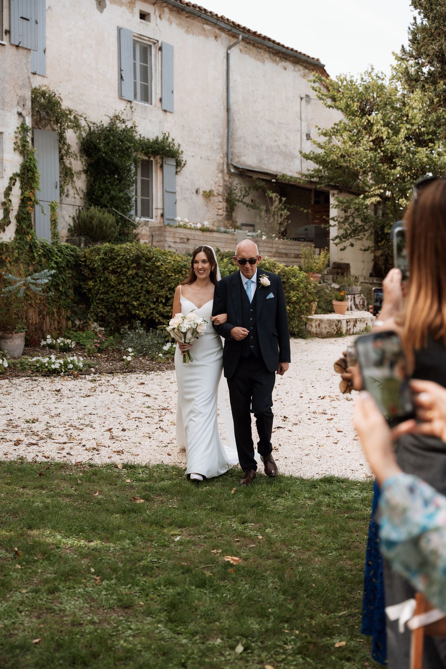Wedding party poses in front of a charming French countryside villa with blue shutters.