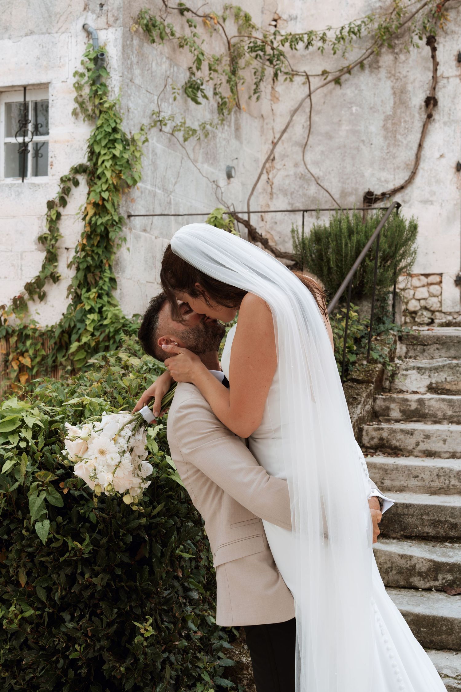Emotional wedding moment captured against a rustic stone wall with climbing vines.