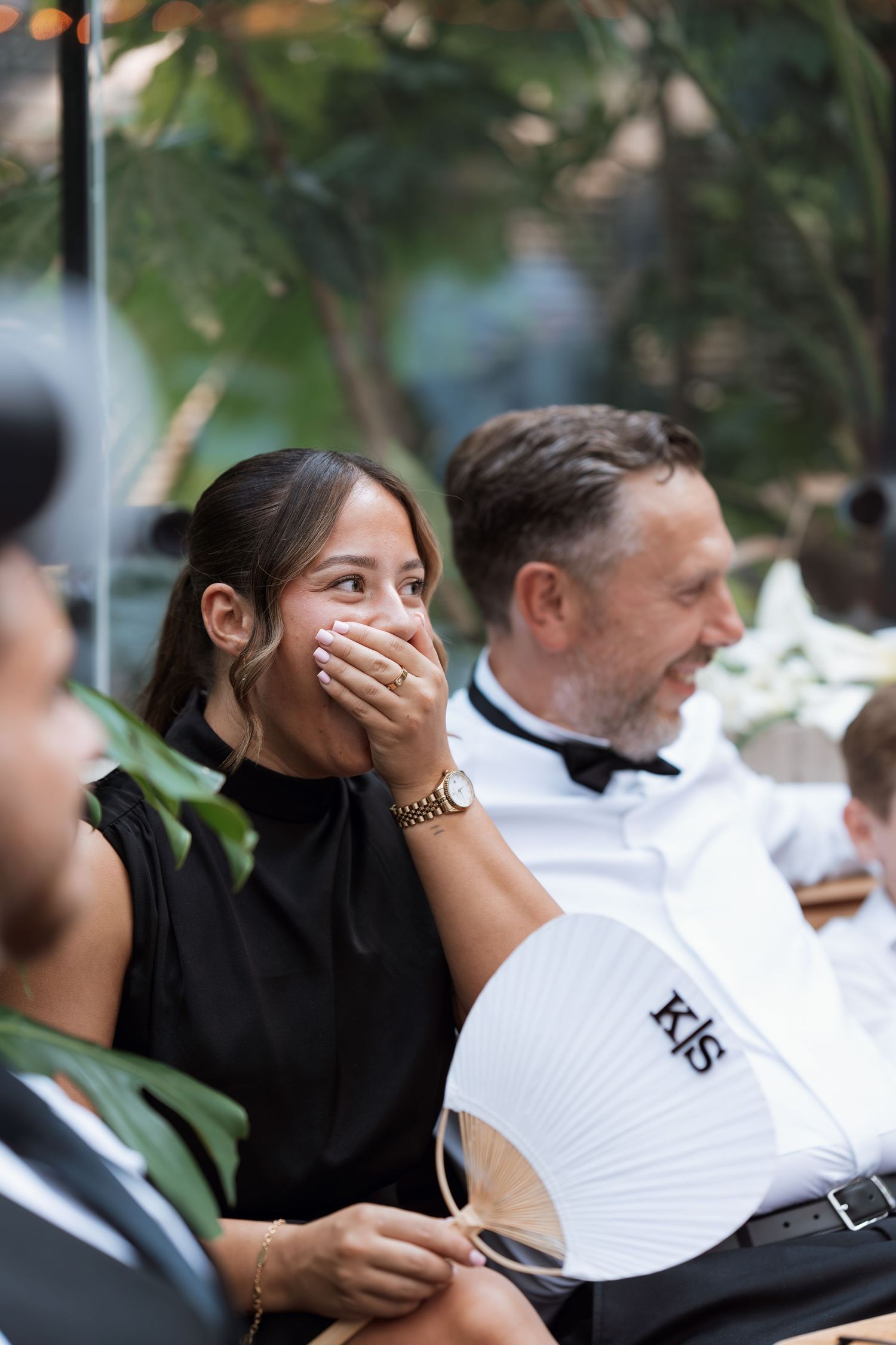 Wedding guests share joyful reactions during an outdoor celebration with tropical greenery.