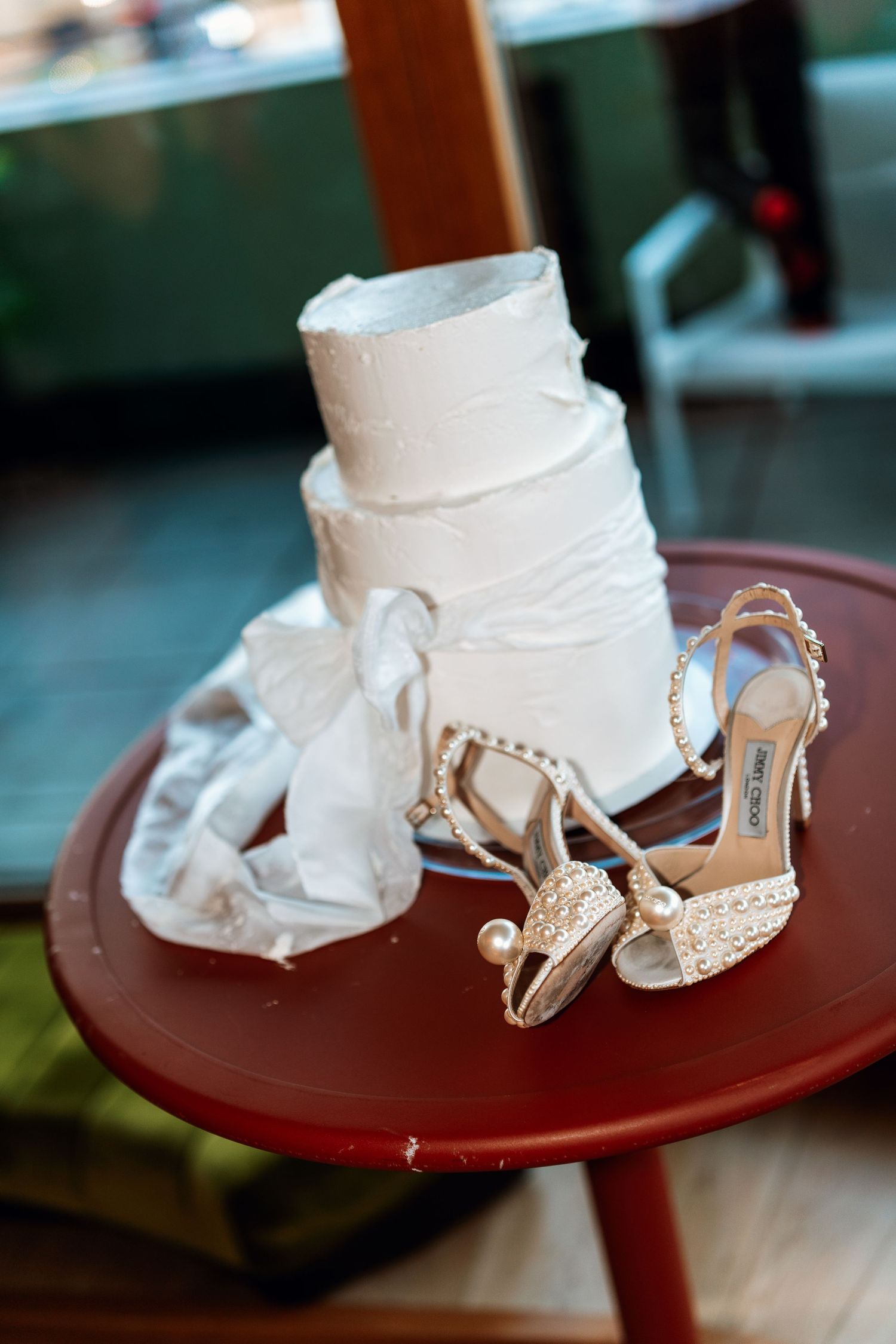 White wedding shoes and fabric displayed on round red table.