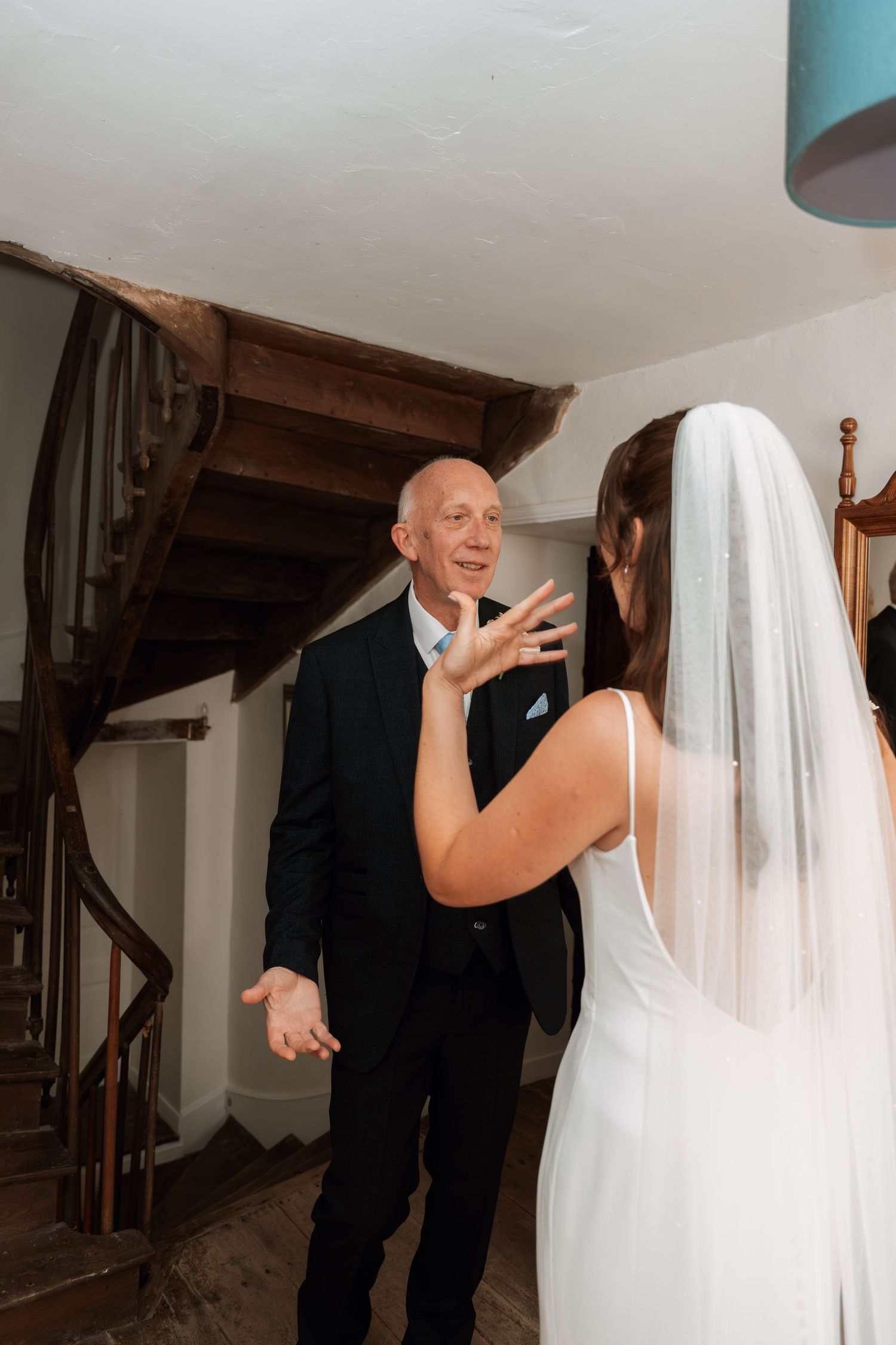 Emotional first look reaction between bride and family member by wooden staircase.