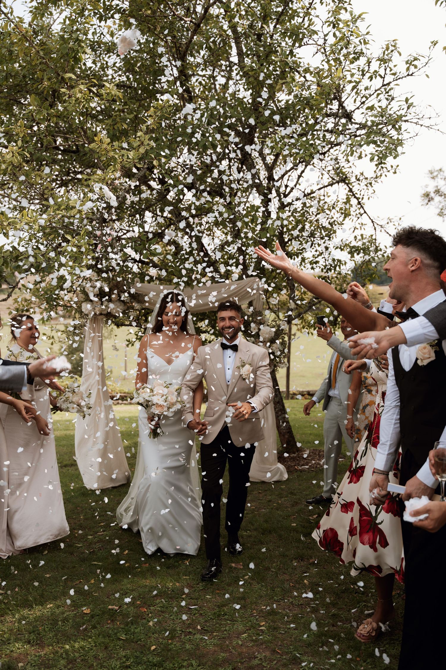 Wedding celebration with confetti being thrown in the air under trees.