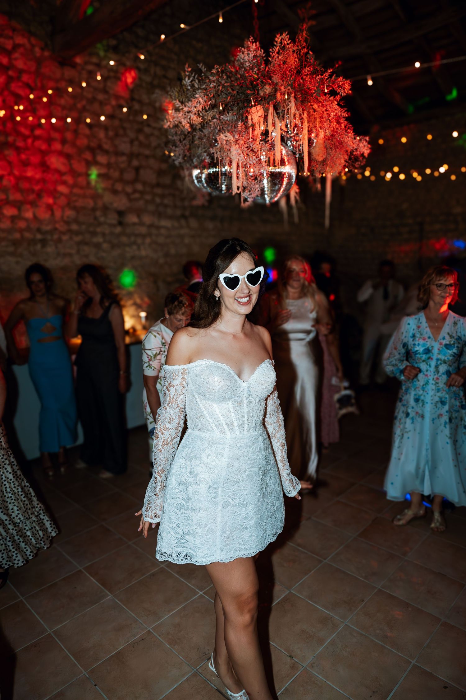 Wedding reception dance floor with festive red lighting and guests dancing in white and blue dresses.
