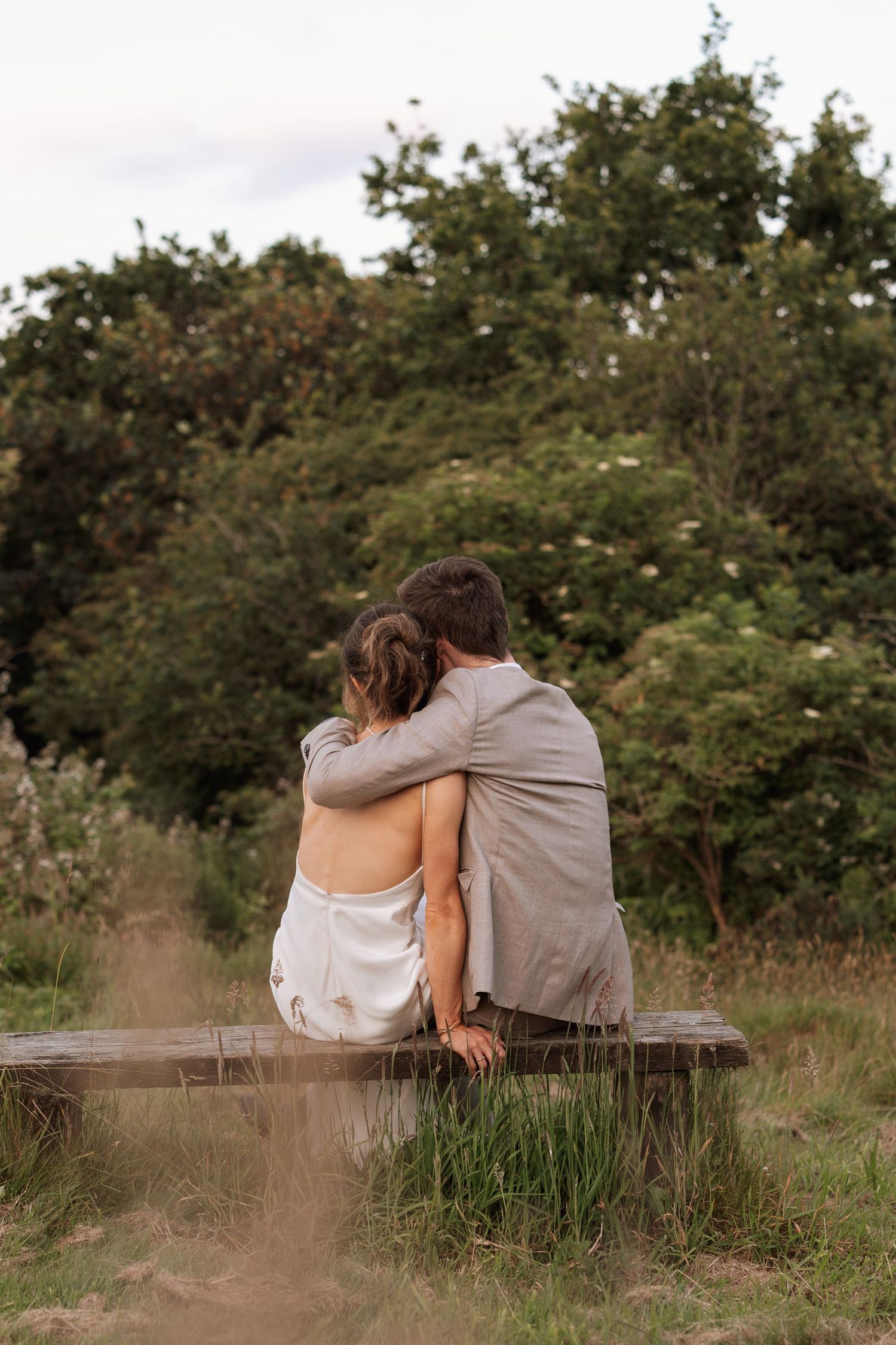 Couple sitting close together on wooden bench in natural outdoor setting.