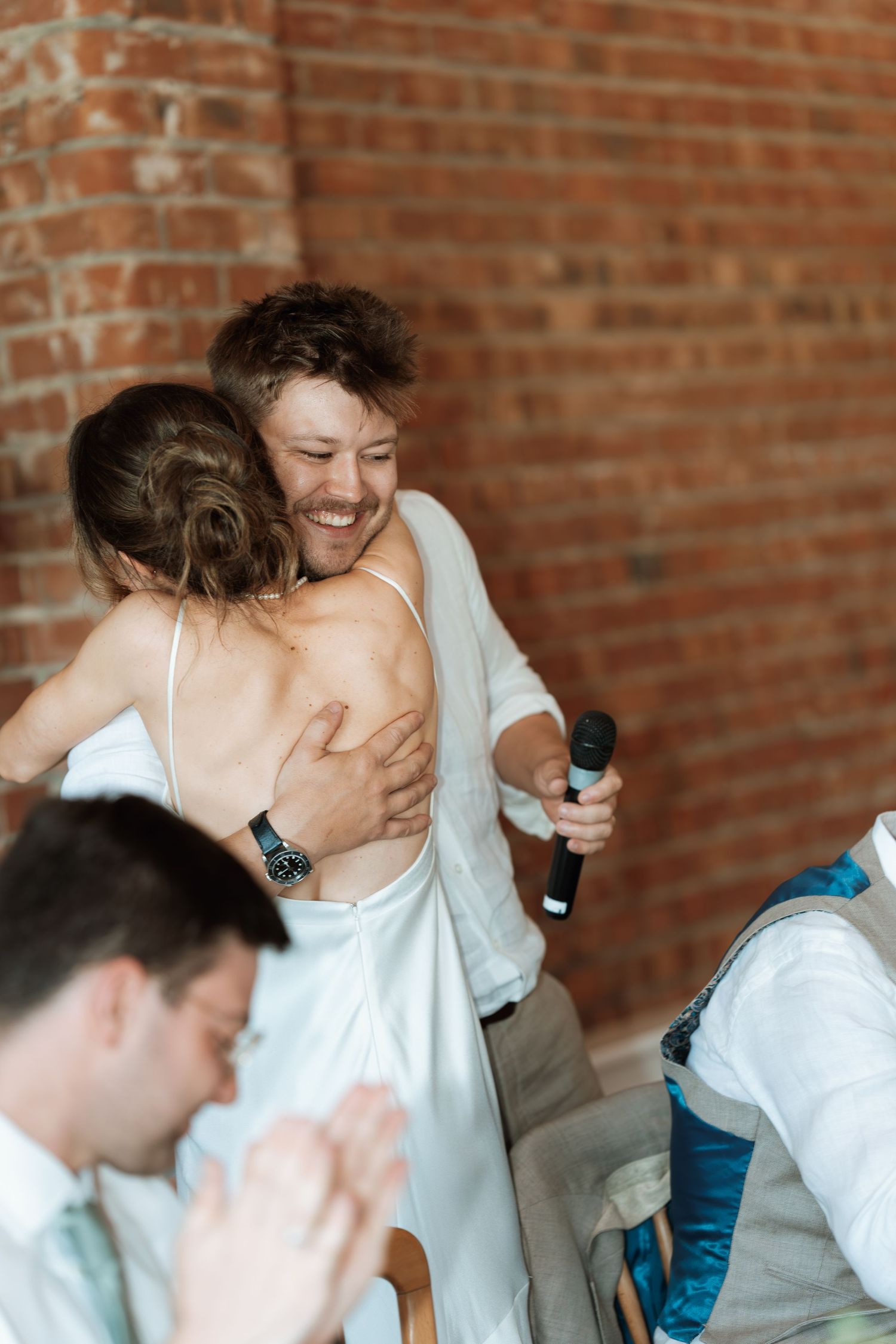 Candid moments of laughter and celebration captured against rustic brick wall background.