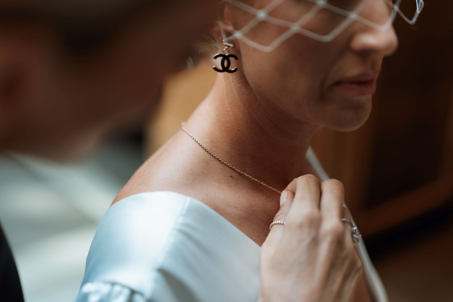 A person wearing a white dress and Chanel earrings poses in elegant bridal attire against a dark background.