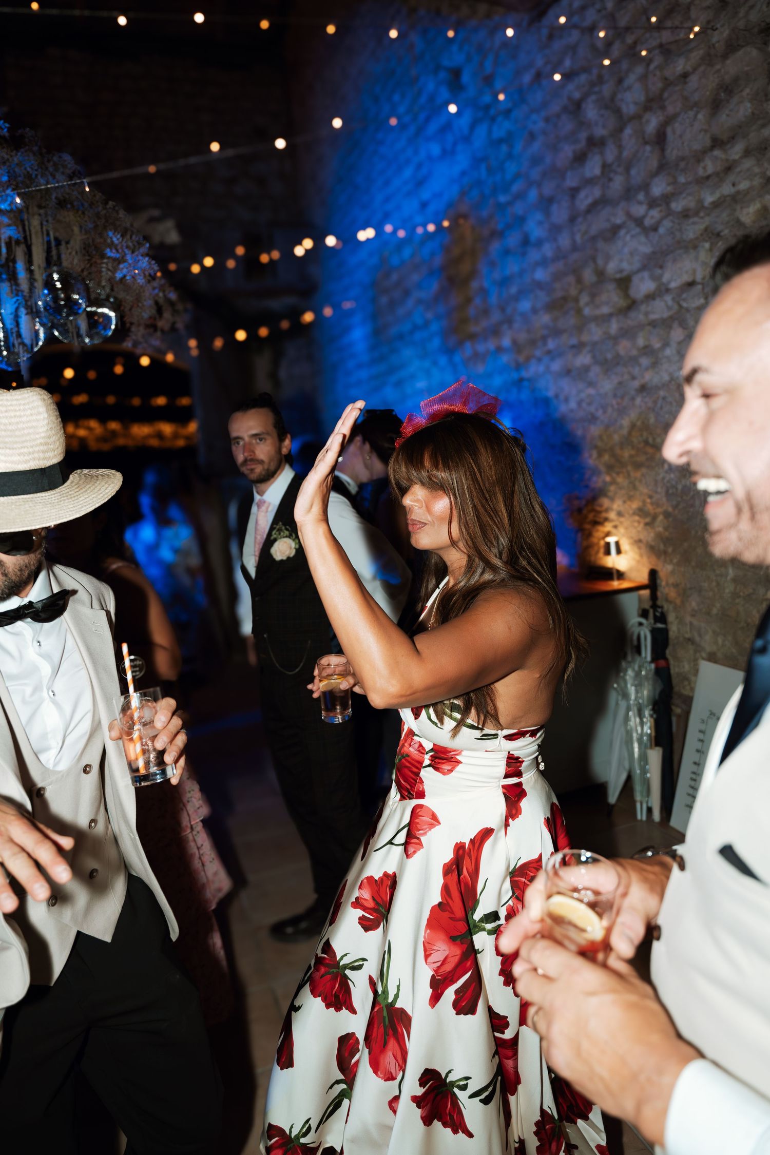 Wedding guests dancing under blue lighting and string lights at reception.