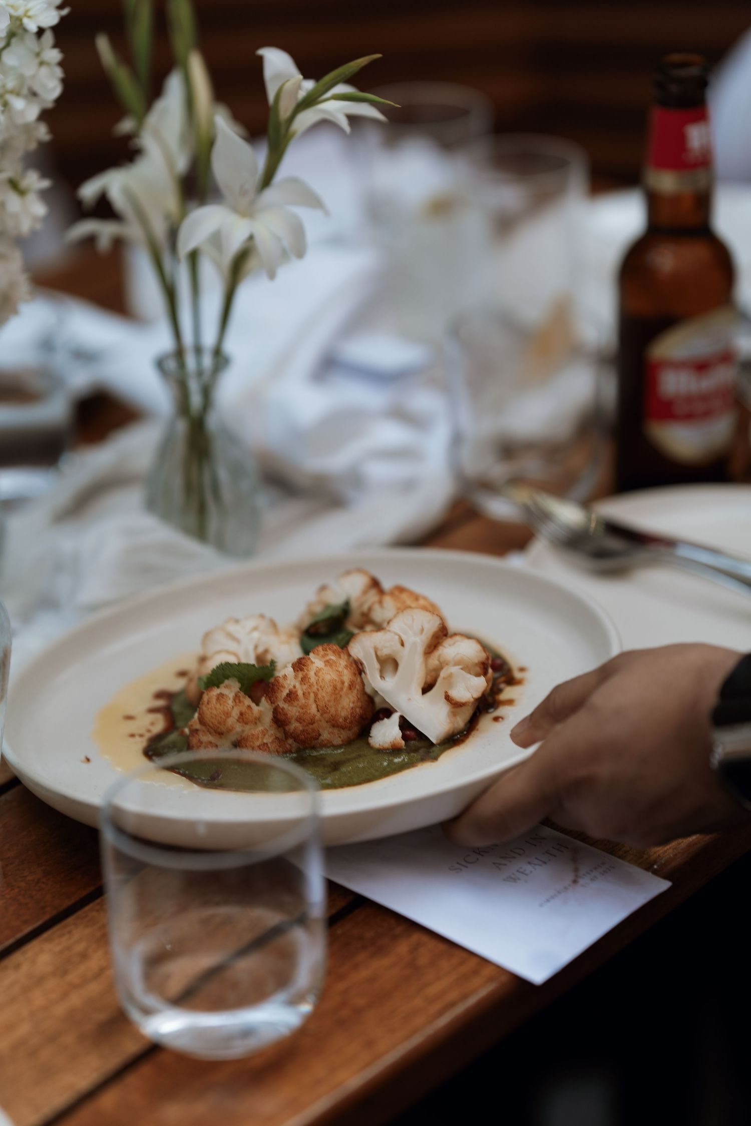 Elegant plated dishes being served on a wooden table with white lilies as centerpieces.